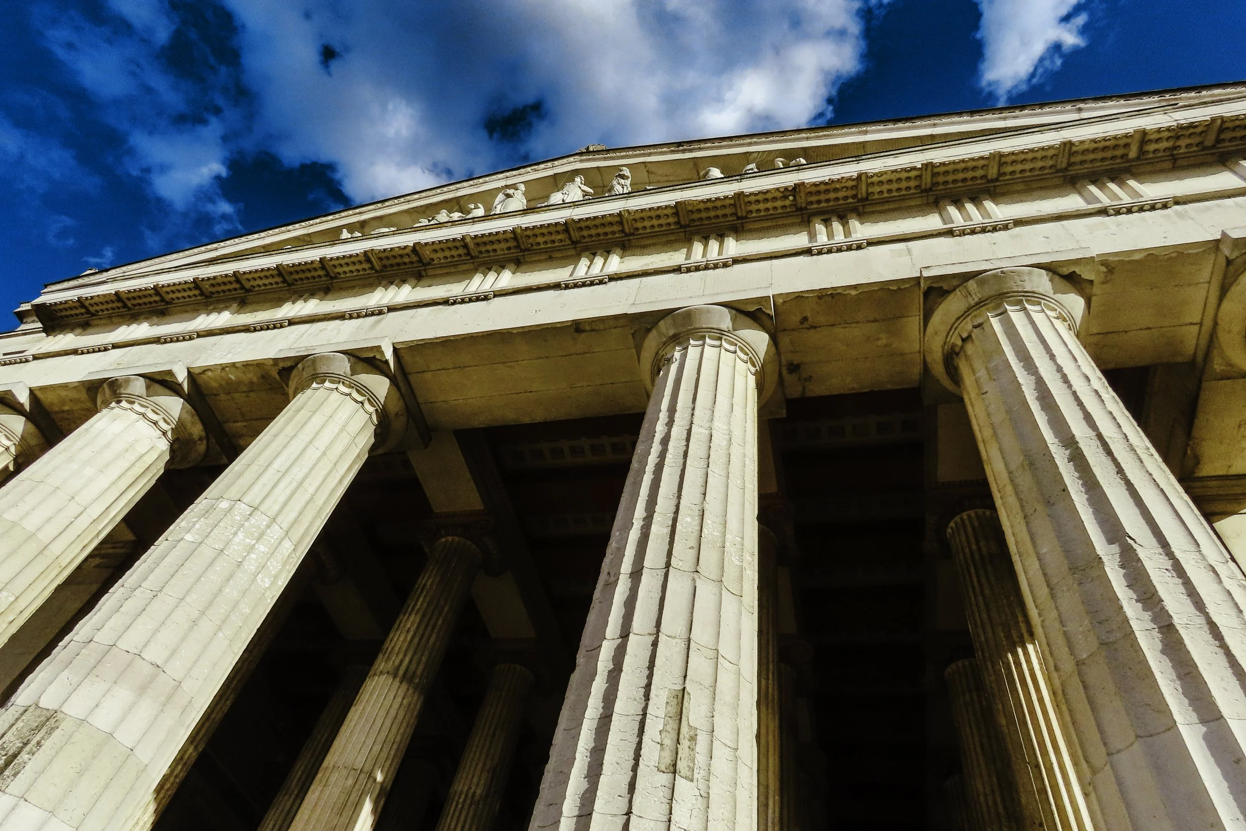 Imperia antica con colonne classiche e architrave, sotto un cielo blu con nuvole