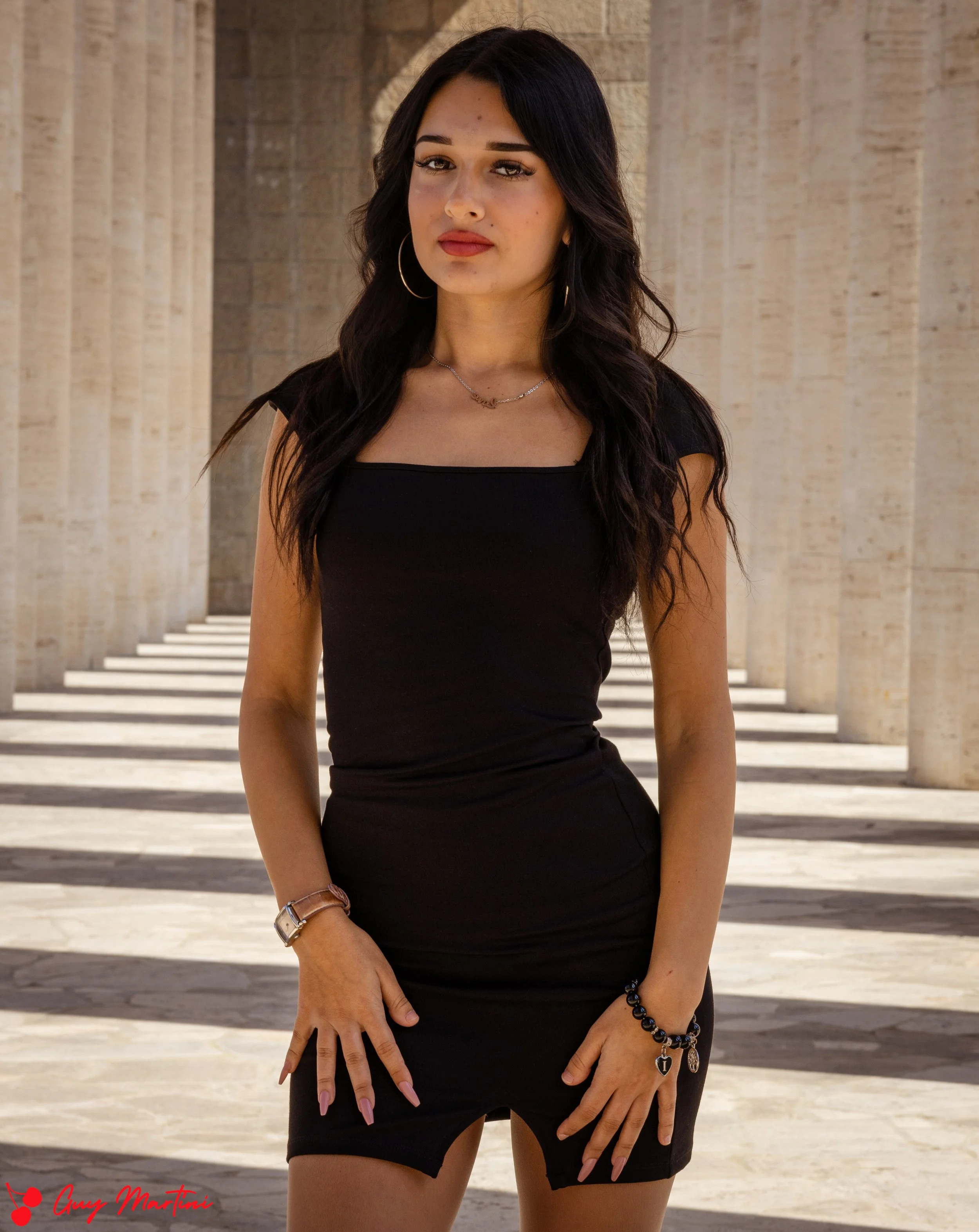 Ragazza con capelli scuri e abbigliamento nero, posa davanti a colonne di pietra in un'architettura classica.