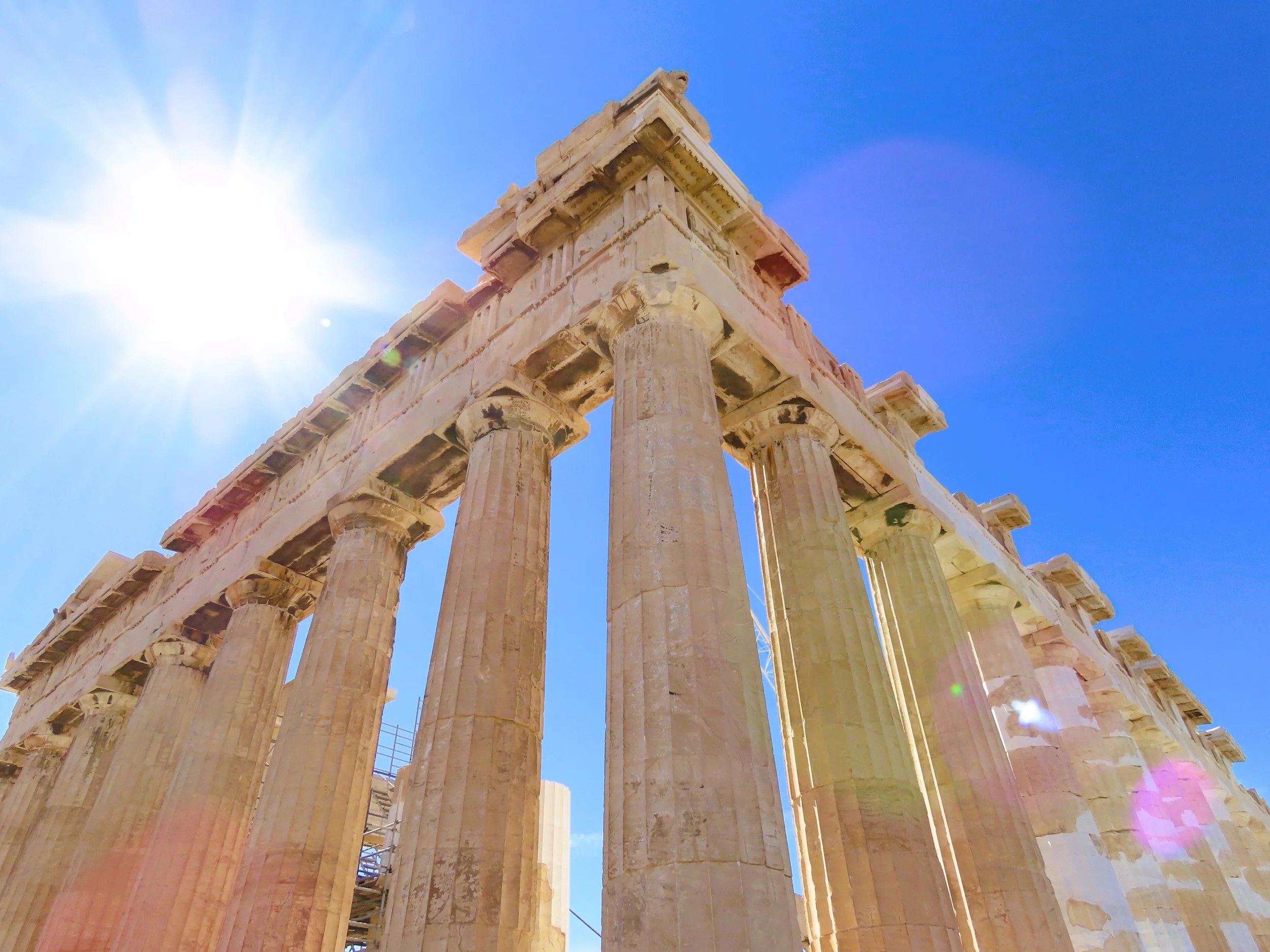 Scalinata del Partenone a Atene con colonne doriche sotto un cielo azzurro e il sole splendente.
