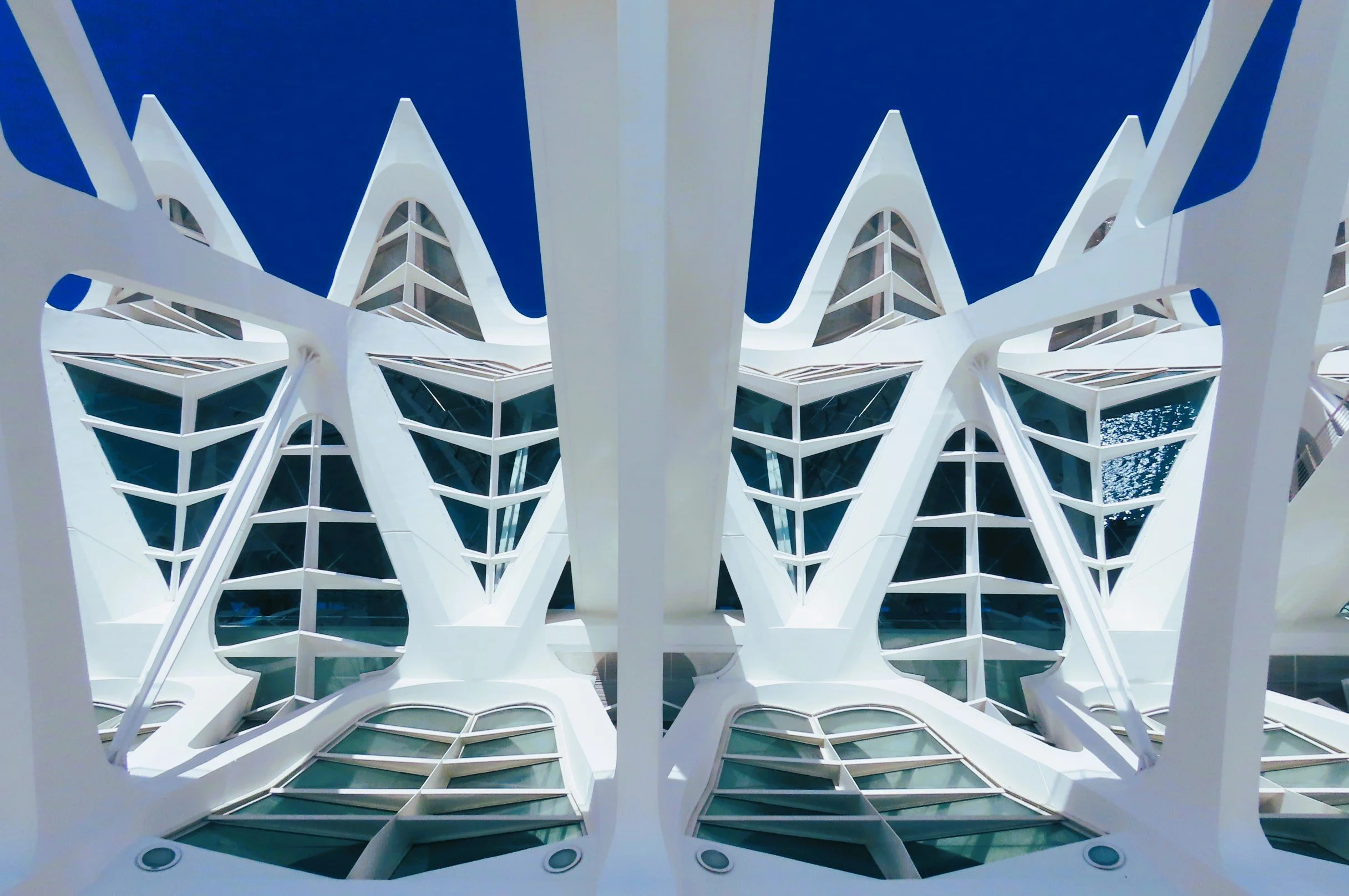 Vista dal basso di un edificio moderno con strutture bianche e grande vetrate, contro un cielo blu.
