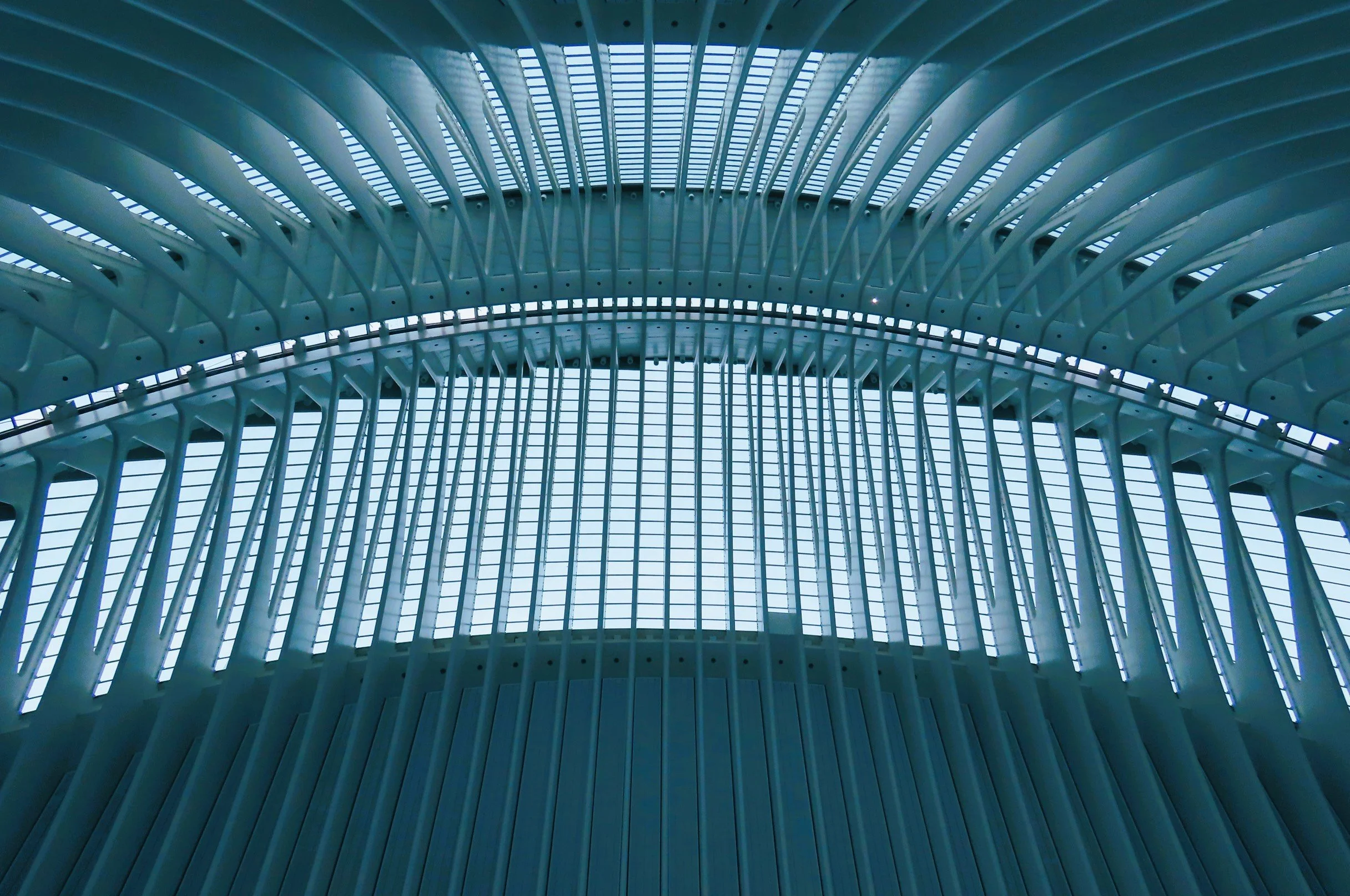 Interno di una struttura architettonica moderna con archi di supporto e vetrate in alto, in tonalità di azzurro e bianco.