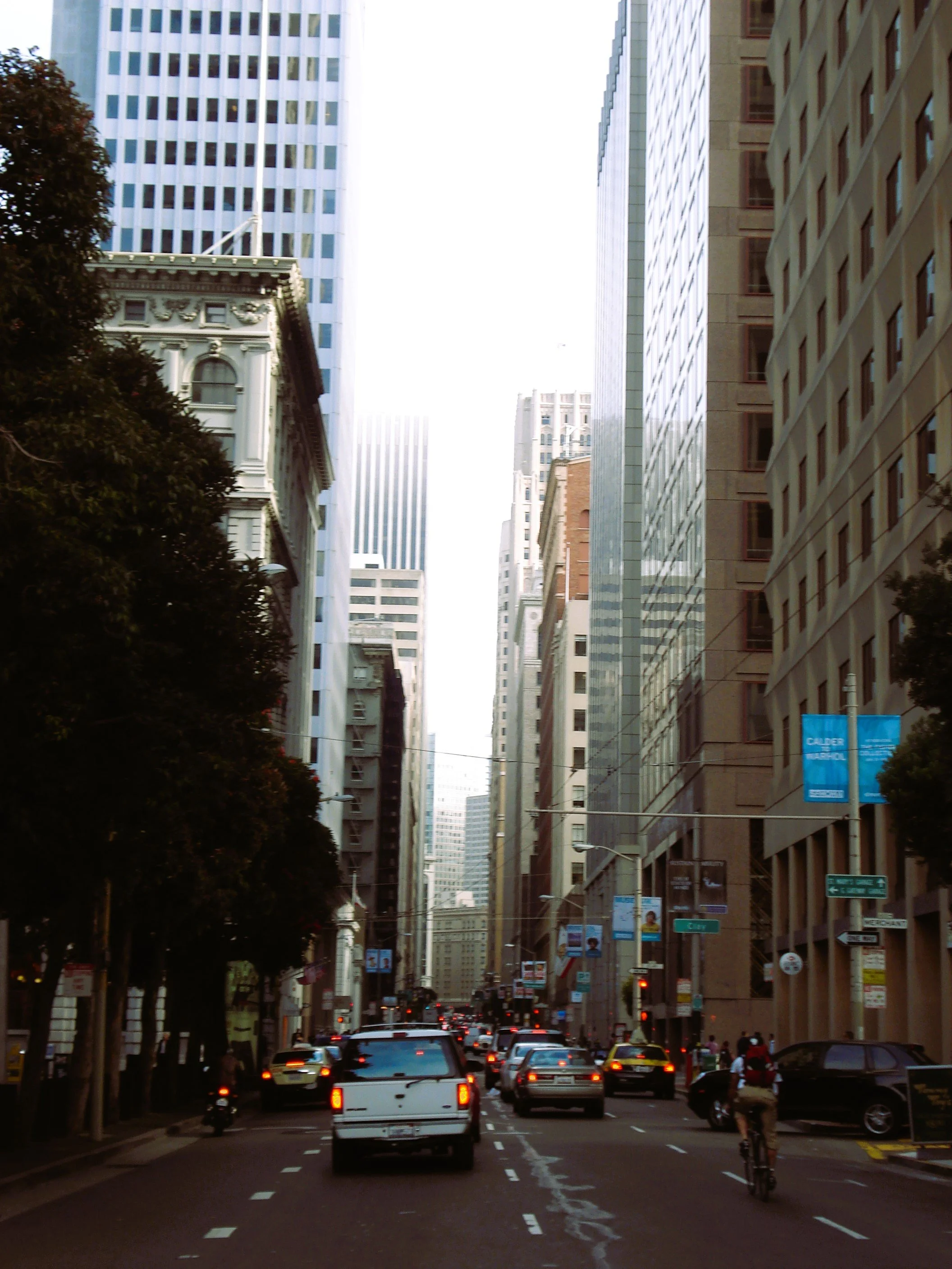 Strada cittadina trafficata circondata da alti edifici con veicoli e ciclisti.