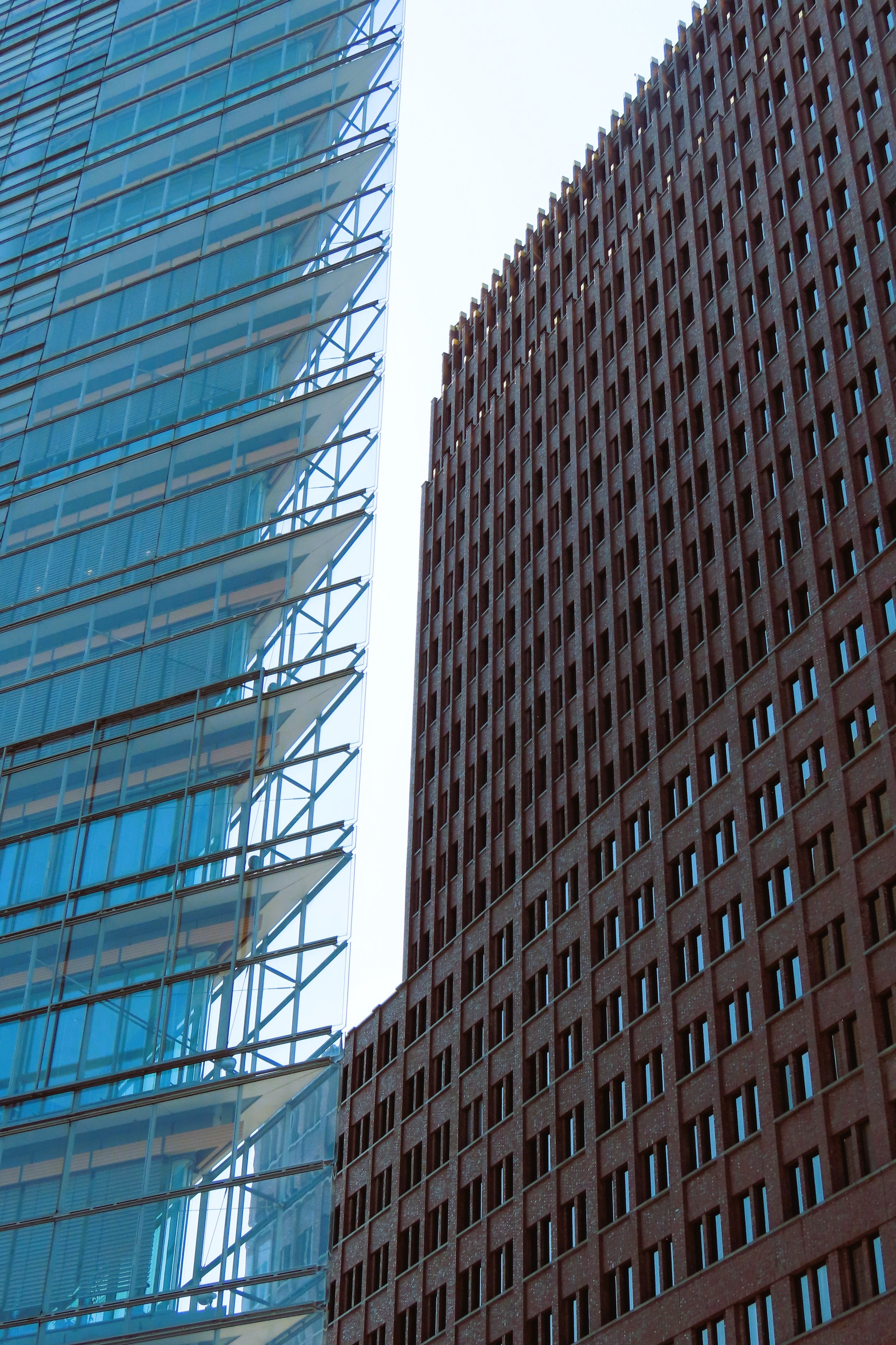 Due grattacieli, uno in vetro blu con strutture in acciaio e l'altro in mattoni rossi, visti dal basso verso l'alto.