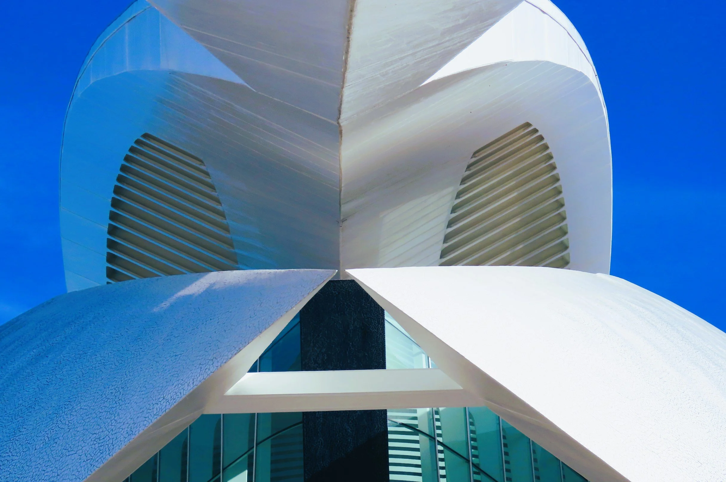 Vista da basso di un edificio moderno con linee curve e facciata in bianco, con un cielo blu sullo sfondo.