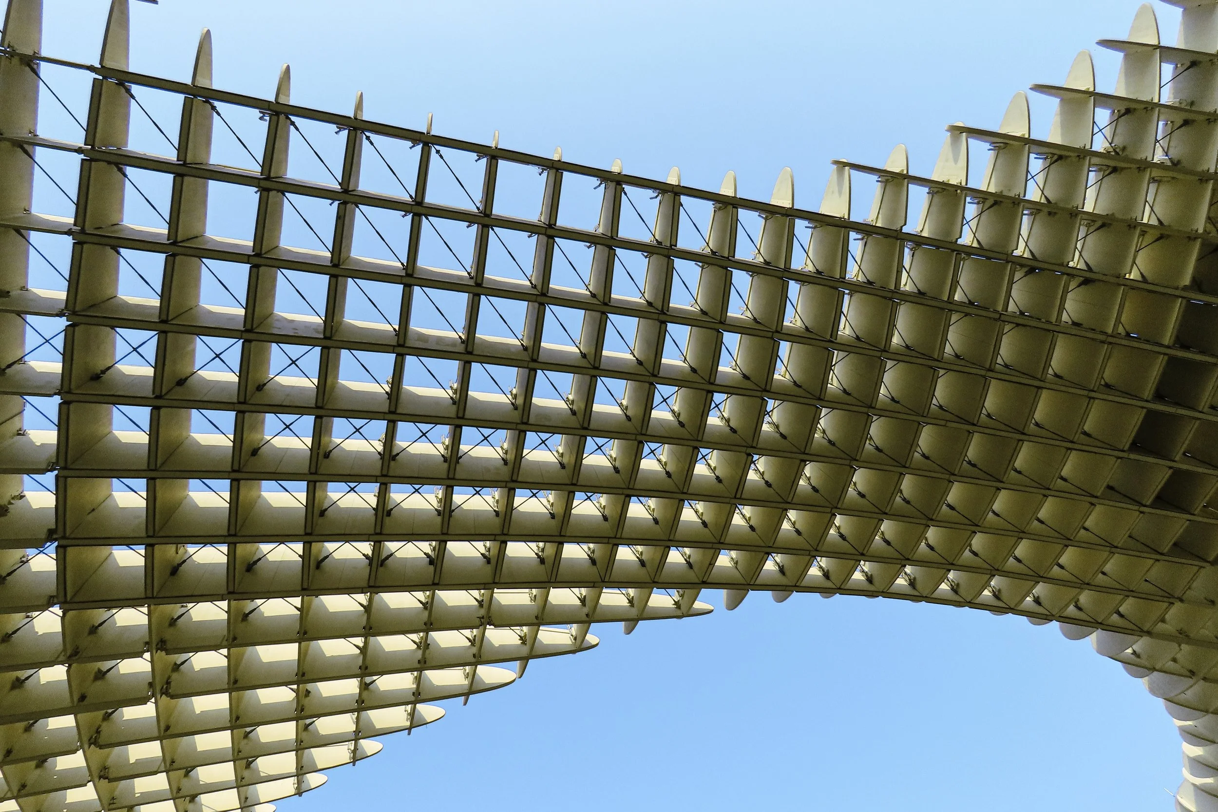 Struttura architettonica moderna con elementi geometrici e una facciata di vetro contro un cielo azzurro.