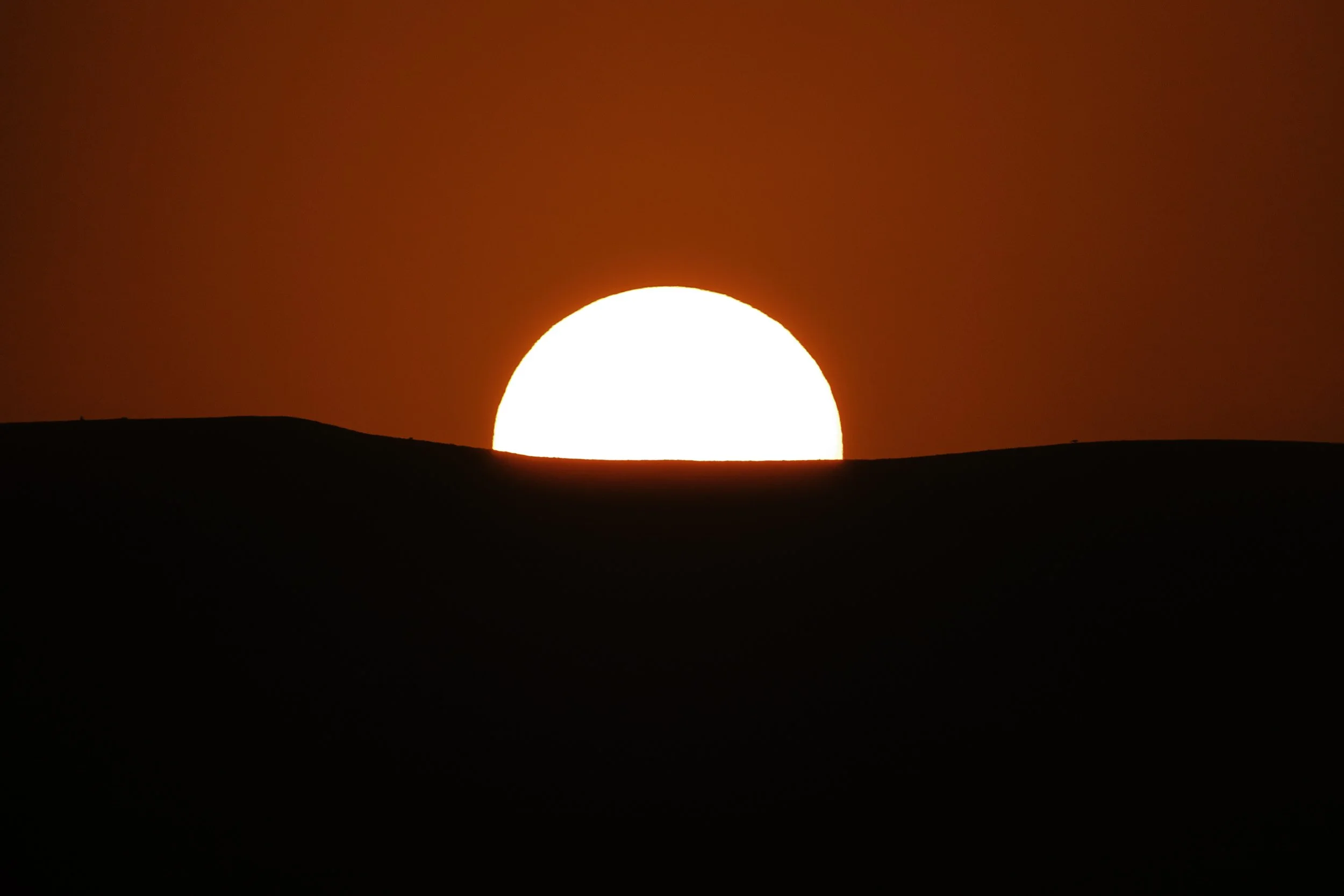 Il sole al tramonto o alba dietro le colline scure, con un cielo rosso intenso.