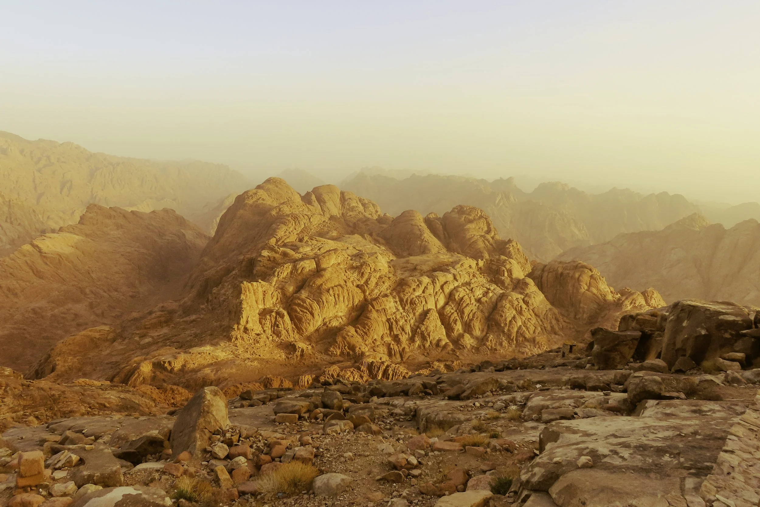 Paesaggio desertico con grandi rocce arancioni e sfondo di montagne illuminato dalla luce del tramonto