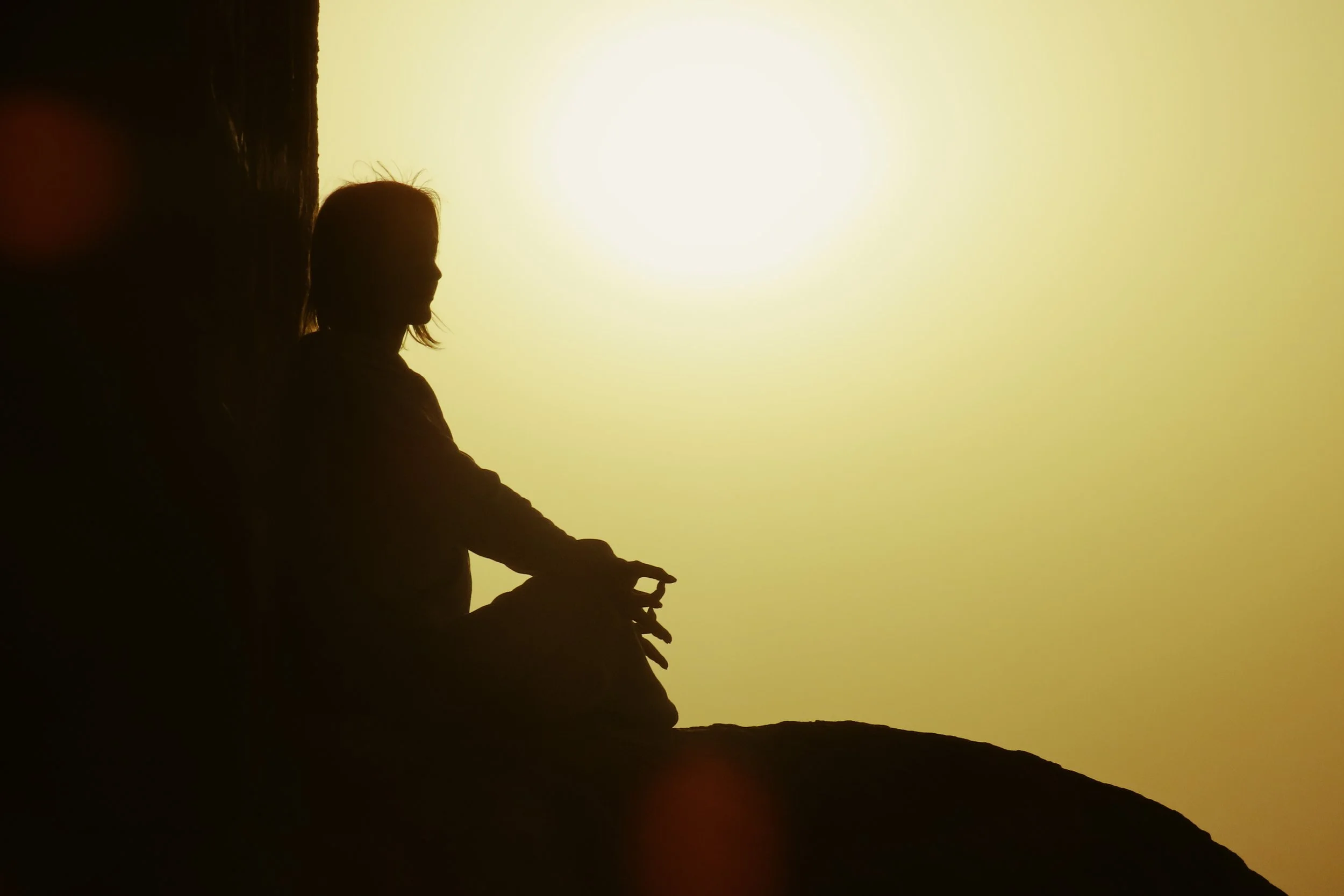 Silhouette di una donna seduta contro una parete, guardando il tramonto.