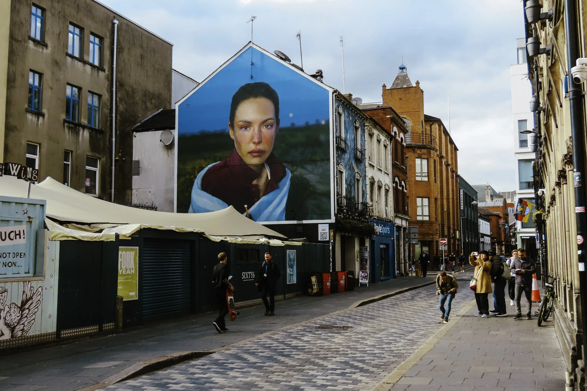 Ragazza con giacca rossa e sciarpa bianca su grande murale su edificio in strada affollata