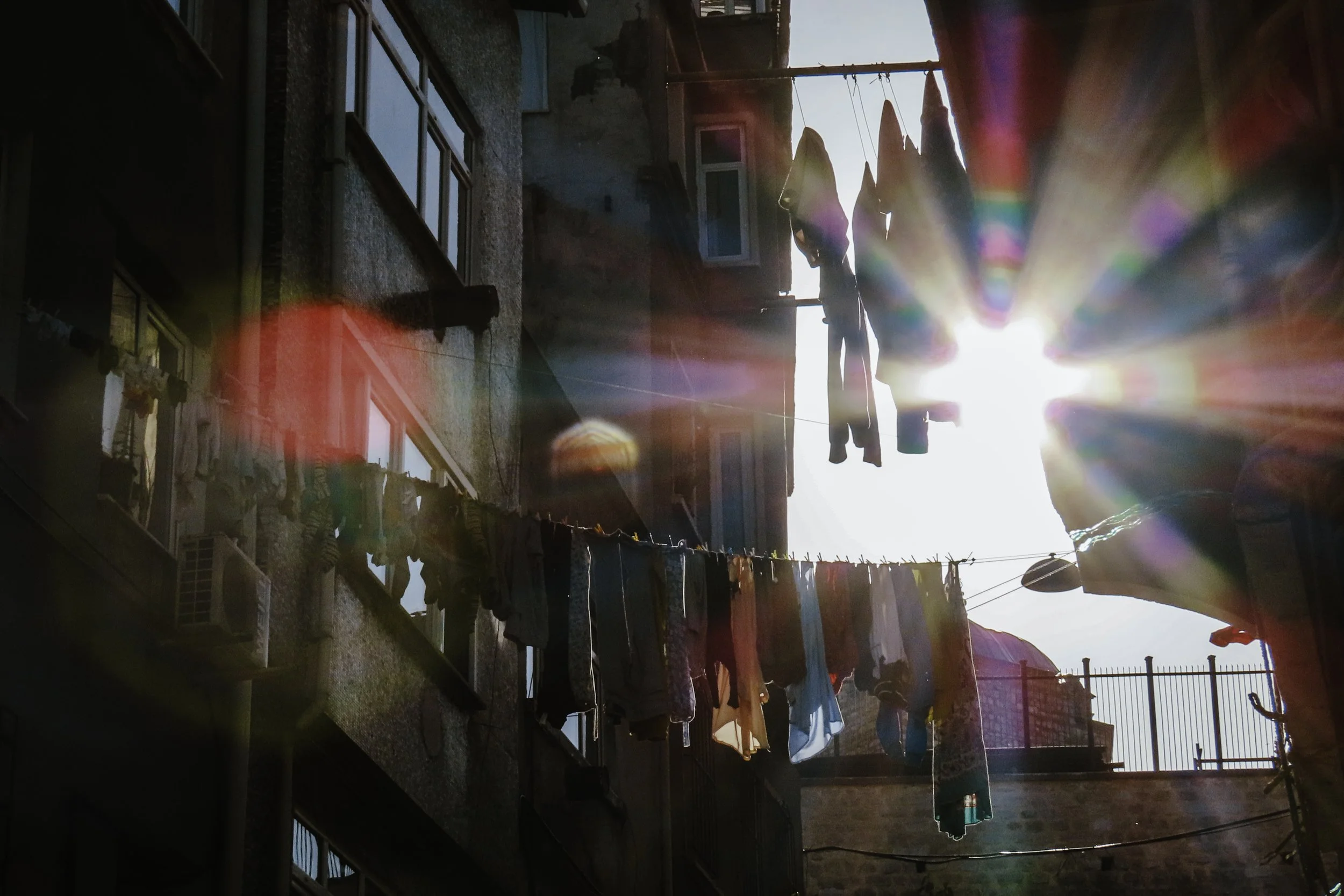 Cortile di un edificio con panni lavati appesi ad un filo, illuminato dalla luce del sole con effetti di lens flare.