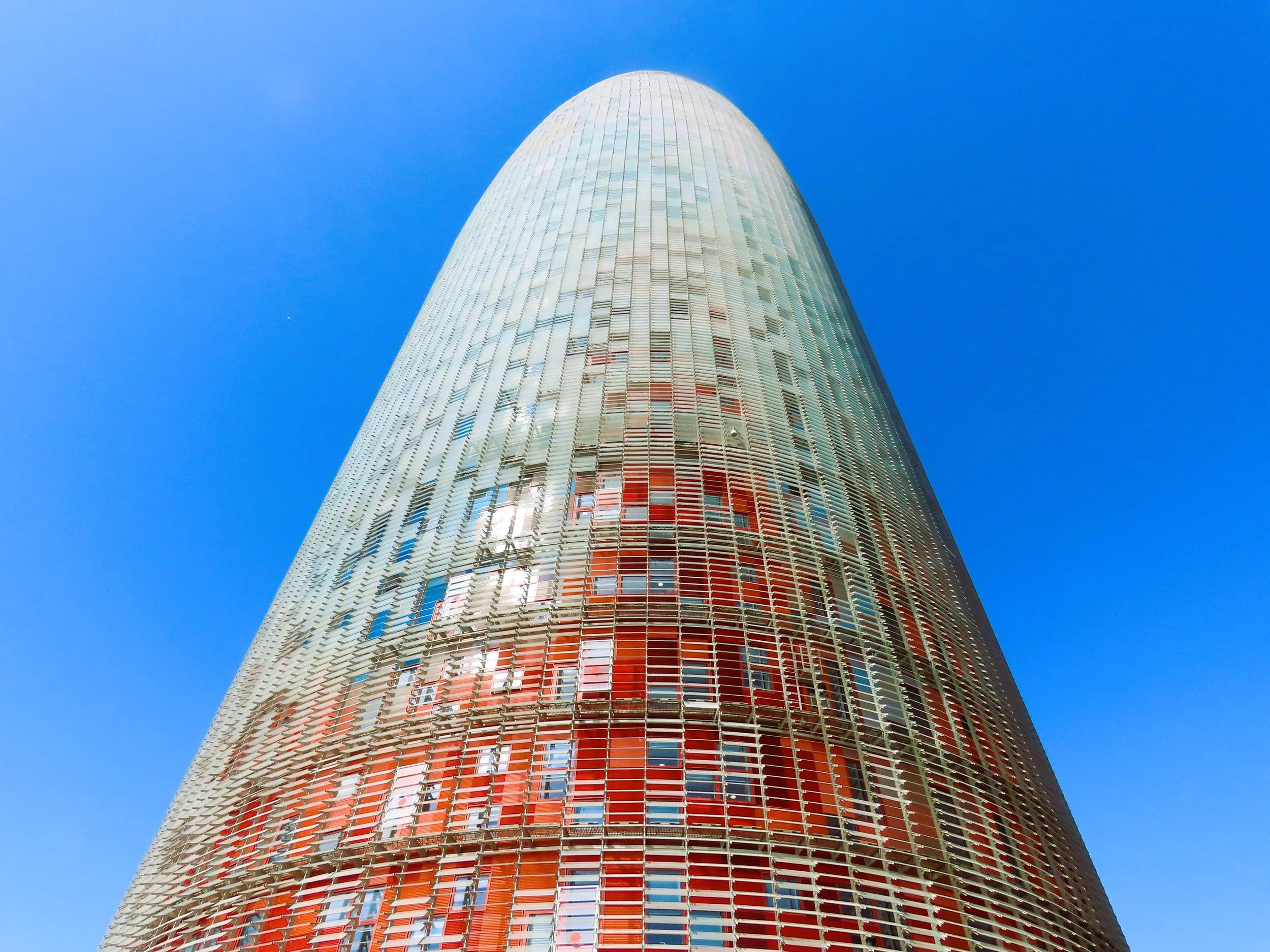 Foto di un grattacielo moderno con una facciata di vetro e un cielo azzurro sullo sfondo.