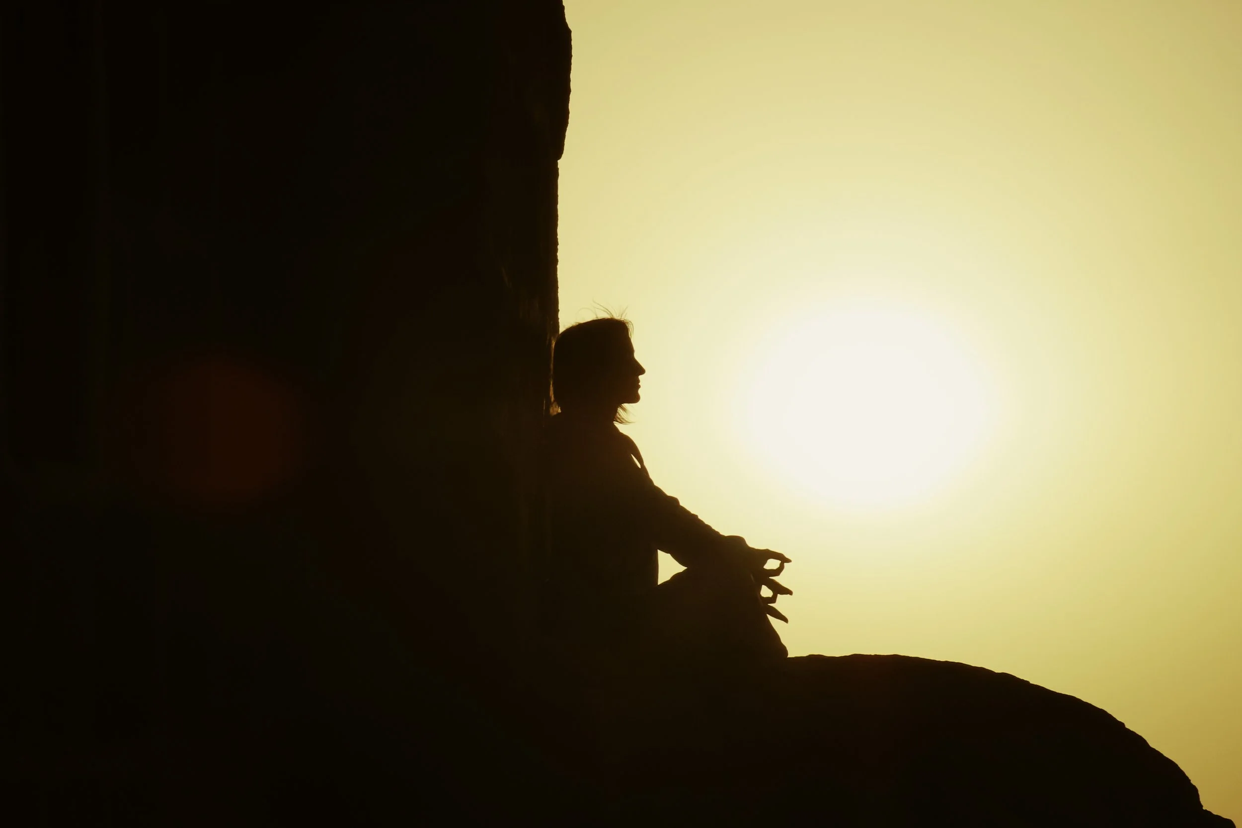 Una donna seduta sulla riva di una scogliera che guarda il tramonto, silhouette contro il cielo caldo.