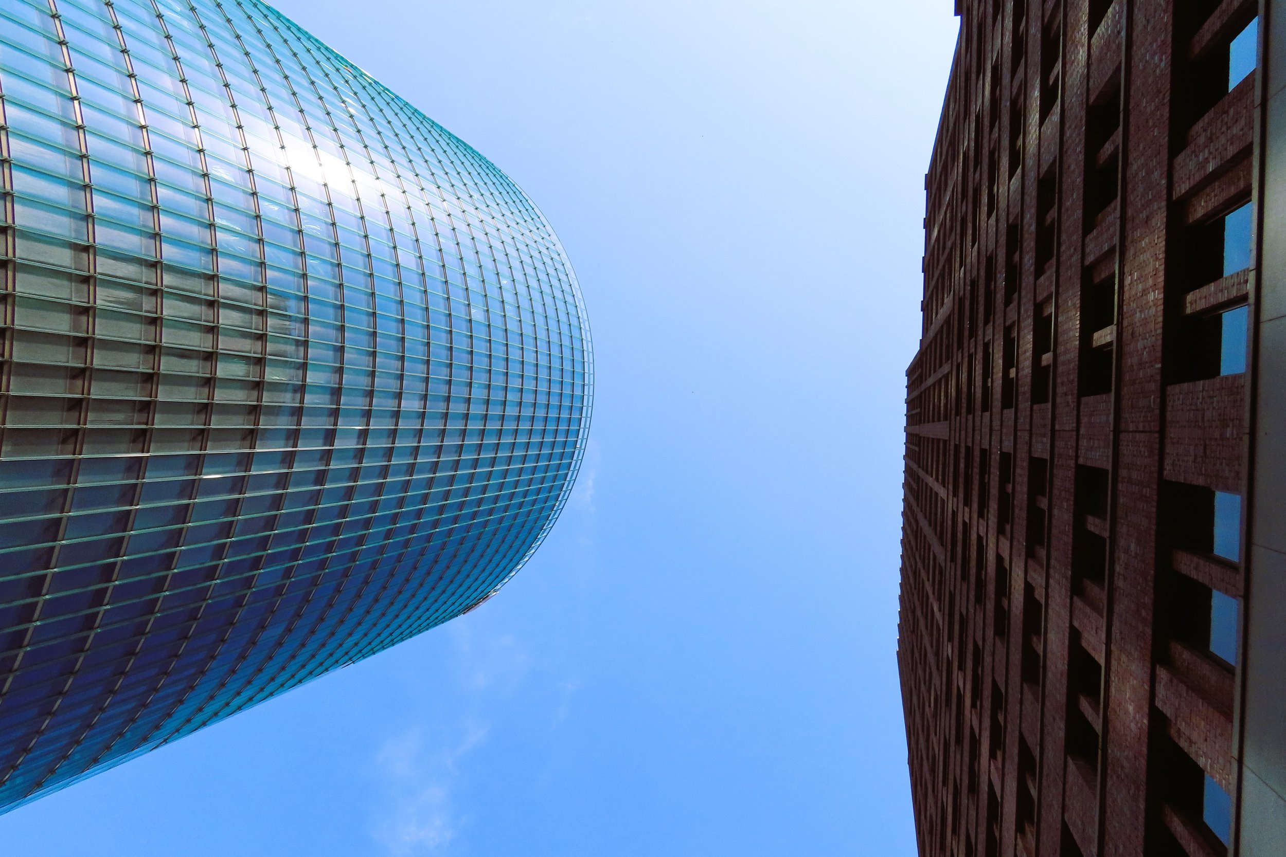 Due grattacieli visti dall'alto verso il cielo, uno in vetro curvo blu e l'altro in mattoni rossi con finestre nere.