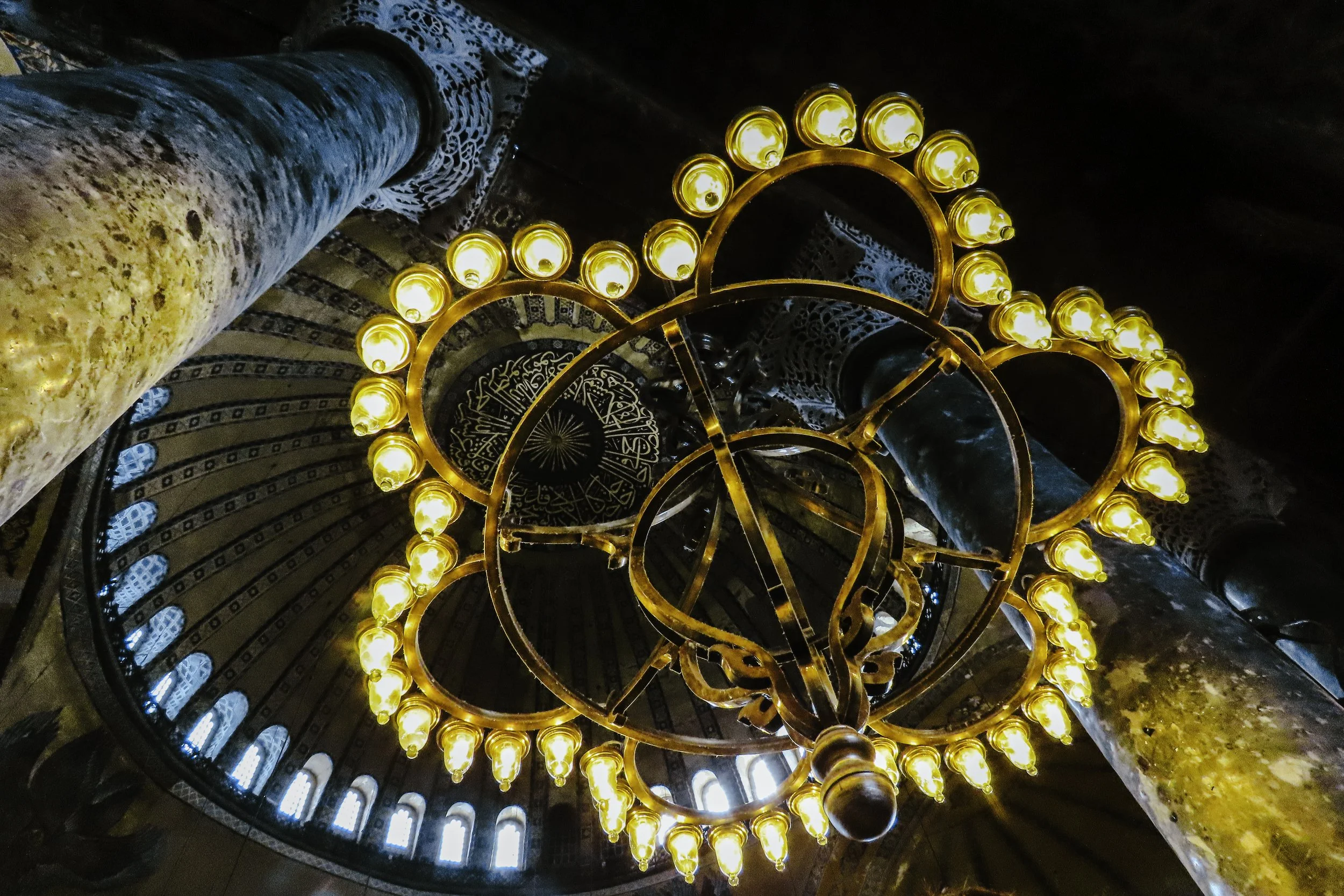 Candelabro a forma di testa di pavone con lucine dorate, visto dal basso con soffitto decorato e colonne in metallo