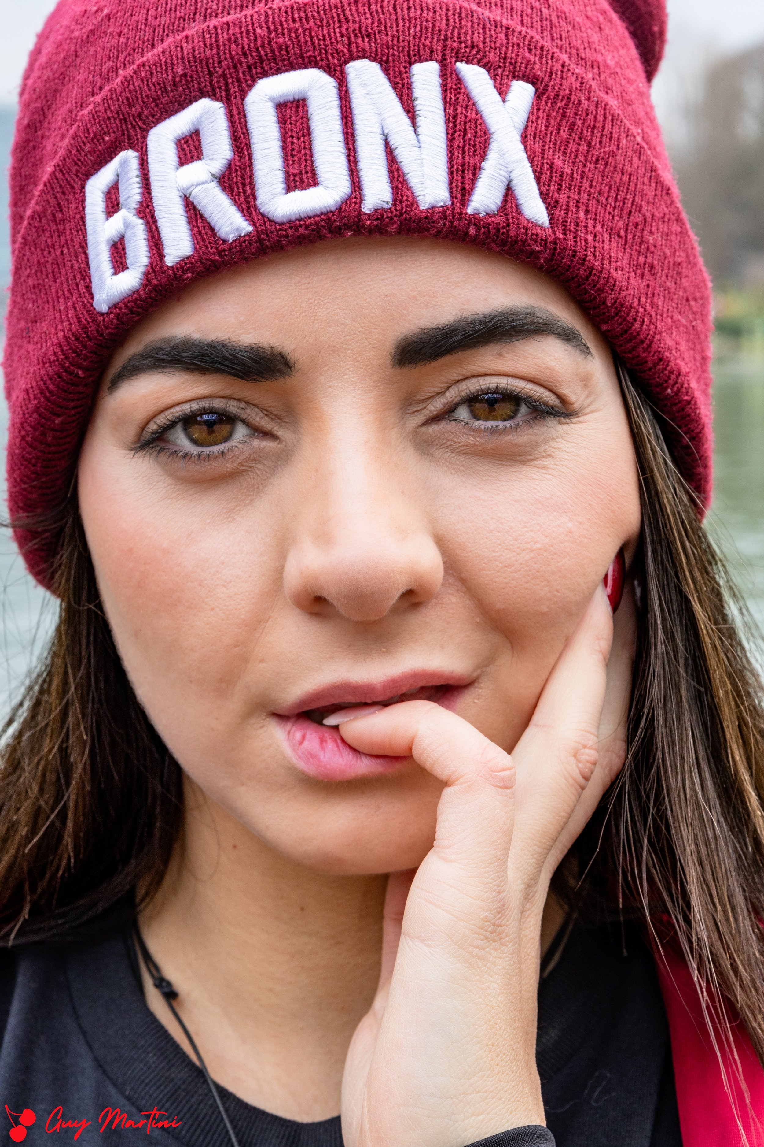 Ragazza con cappellino rosso con scritta bianca 'Bronx', che si tocca il viso con una mano.