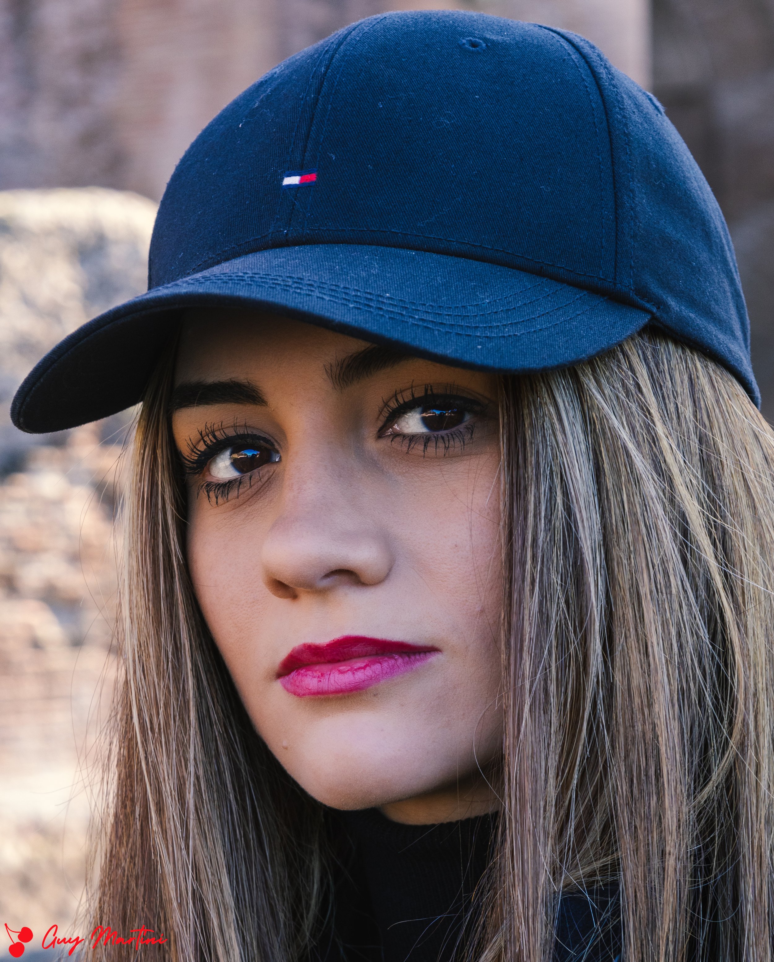 Ragazza con cappello blu, capelli castani lisci, trucco chiaro, labbra rosa, sfondo naturale