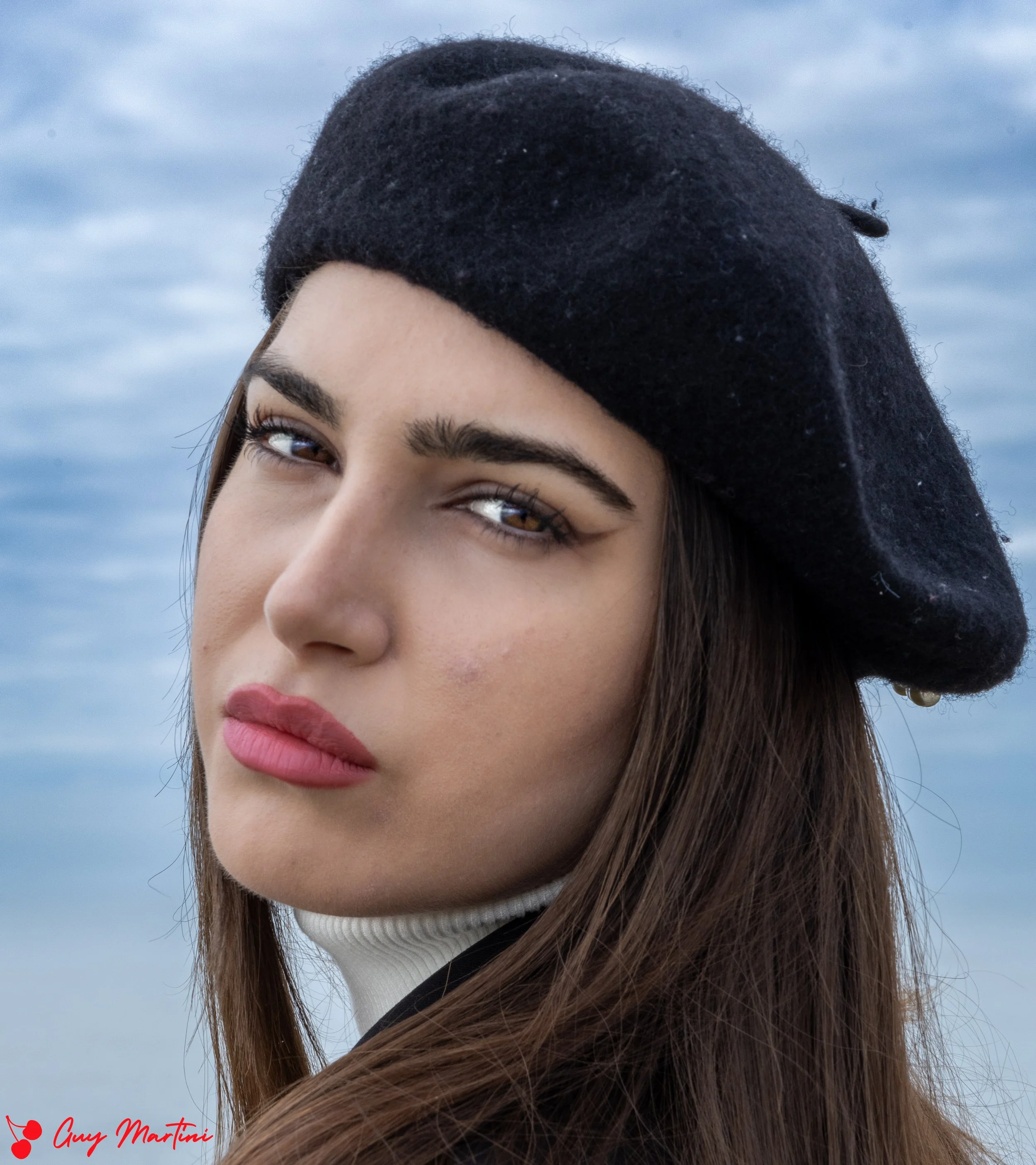 Ragazza con cappello nero che guarda verso l'obiettivo con uno sfondo di cielo nuvoloso.