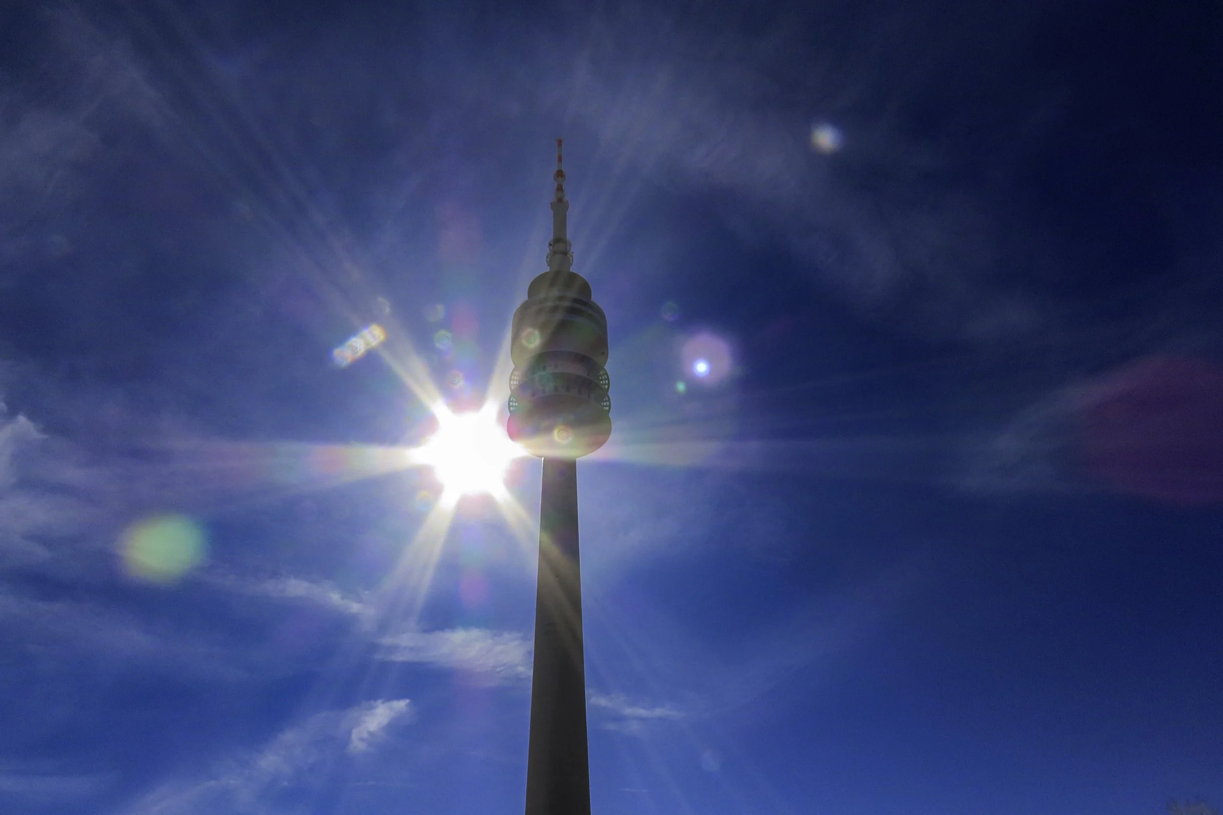 Torres di comunicazione alte contro un cielo blu con il sole che splende dietro, creando un effetto di lens flare.