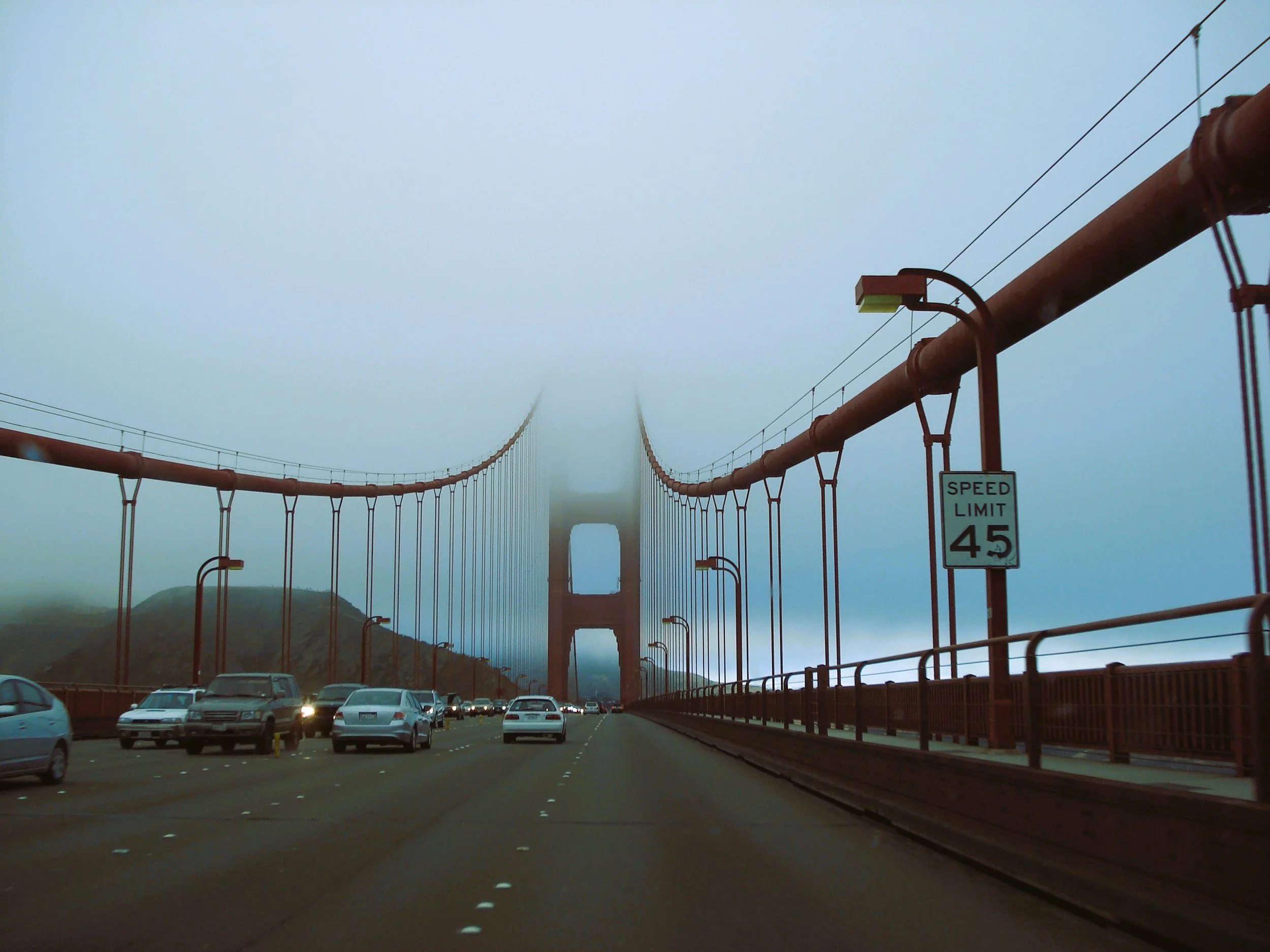 Vista del Golden Gate Bridge avvolto nella nebbia con auto in movimento e un cartello di limite di velocità di 45 mph.