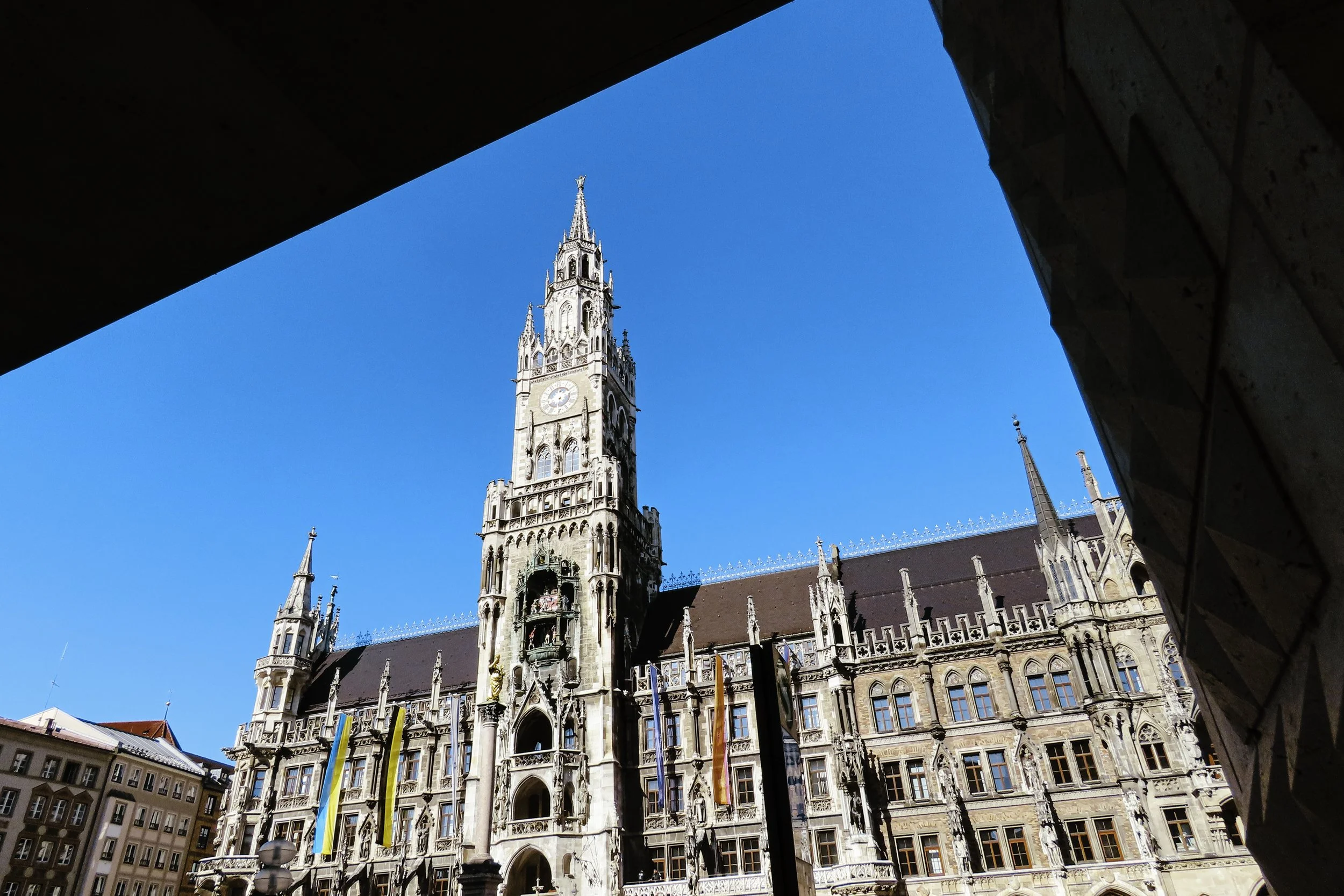 Vista della Torre del Municipio di Monaco di Baviera vista attraverso un'apertura, con un cielo azzurro come sfondo.