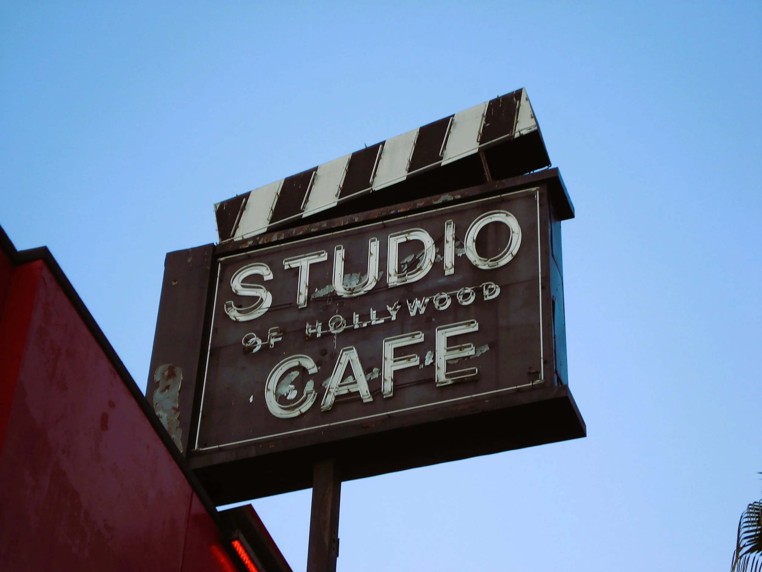 Insegna in stile vintage con scritte luminose: 'Studio of Hollywood Cafe', con strisce bianche e nere sulla parte superiore.