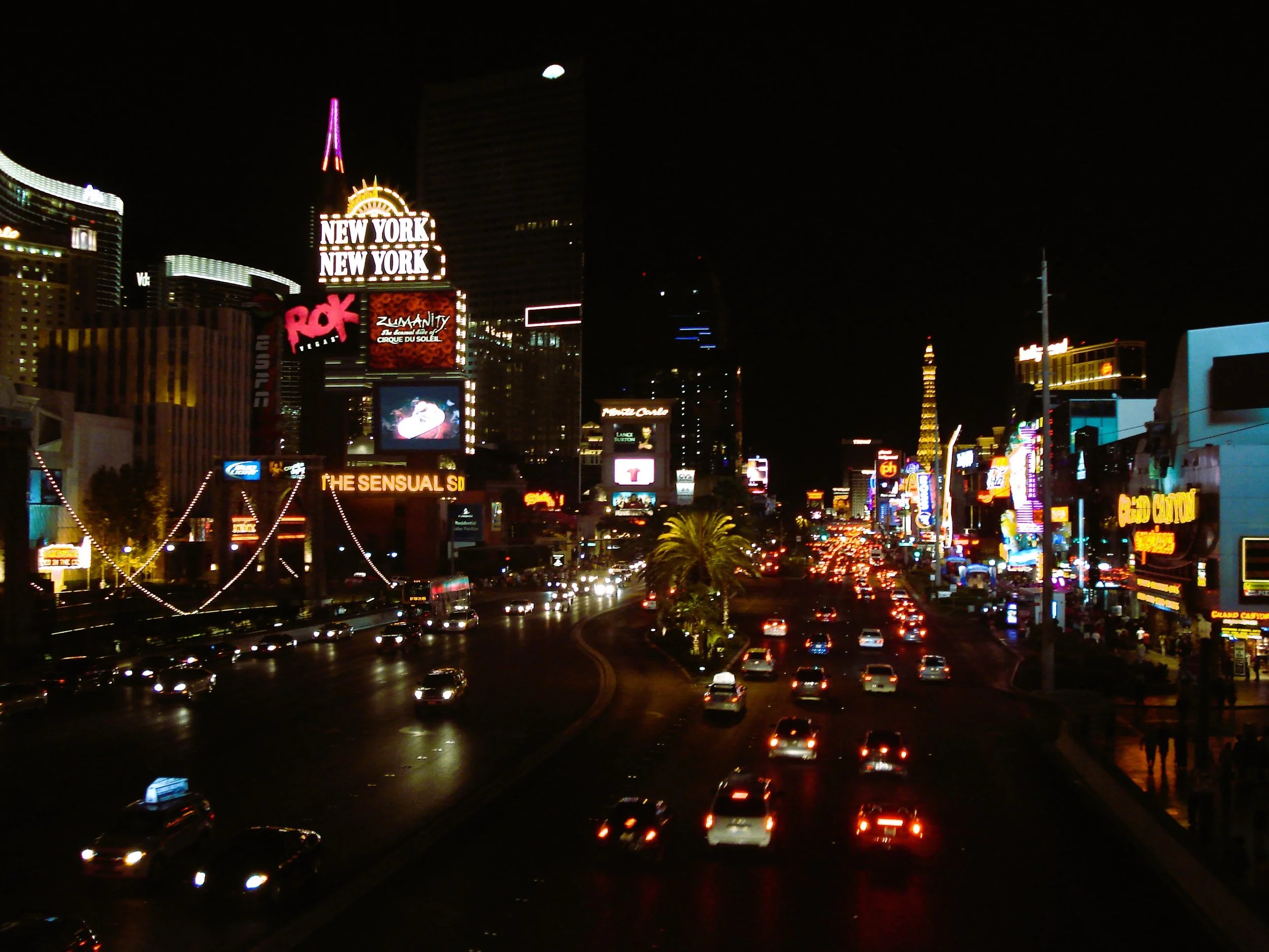 Vista della Strip di Las Vegas di notte con luci e insegne pubblicitarie colorate, e il famoso hotel Paris con la Torre Eiffel in fondo.