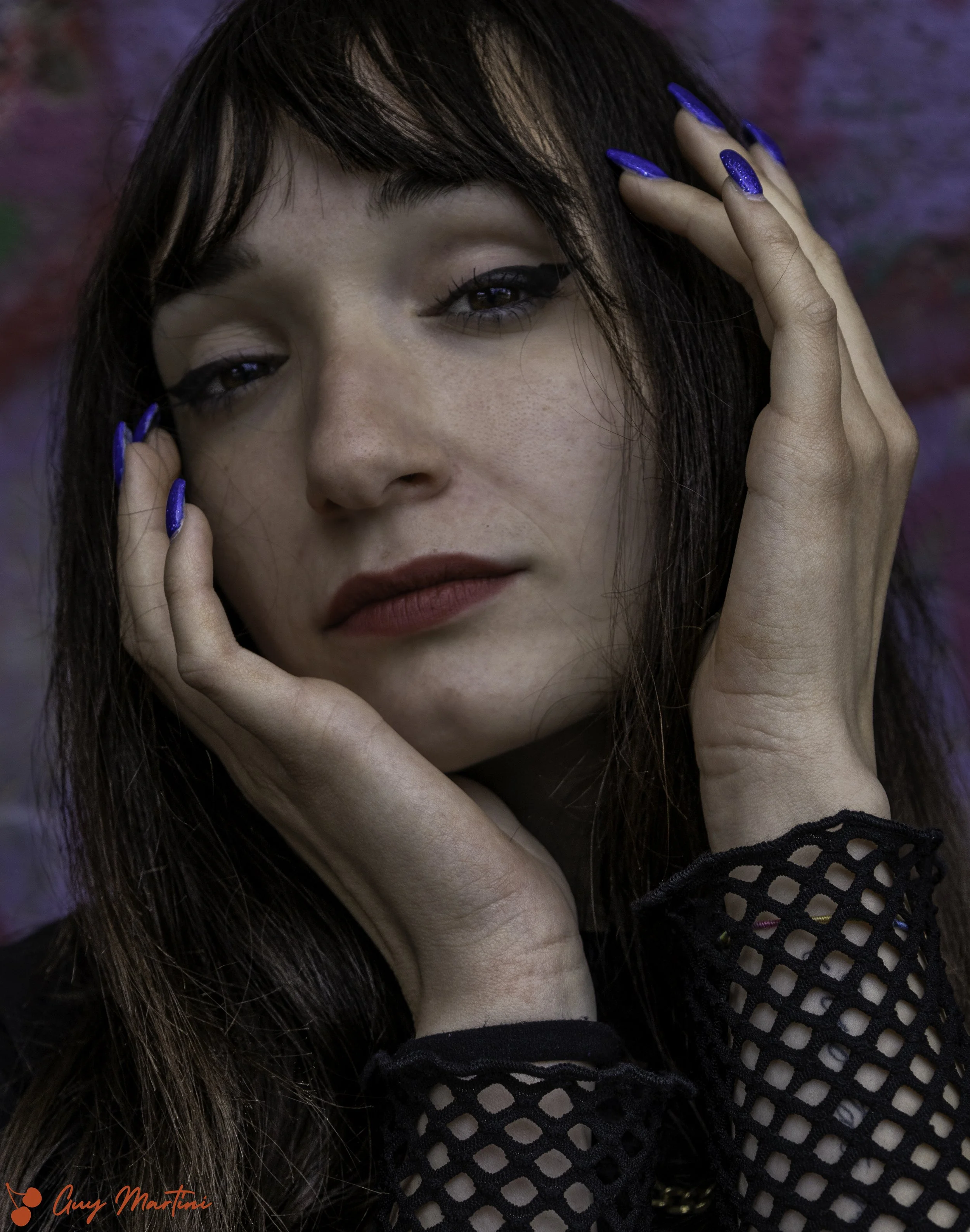 Ragazza con capelli castani e occhi azzurri che indossa smalto blu e un top nero con motivo a rete.