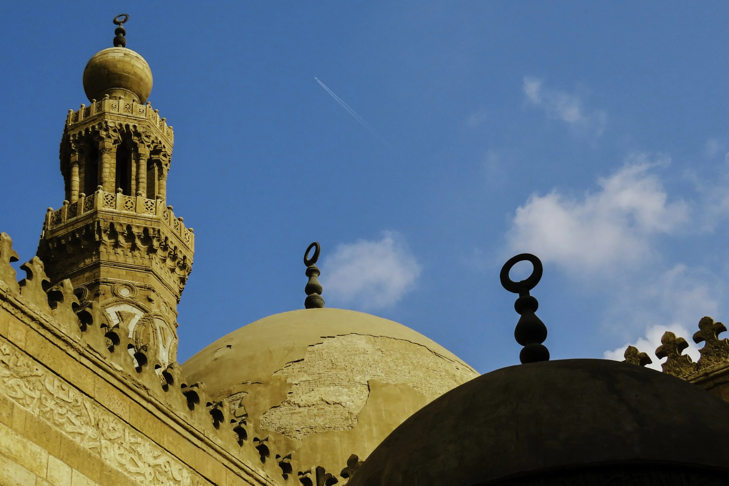 Particolare di un minareto e della cupola di una moschea con il cielo azzurro sullo sfondo.