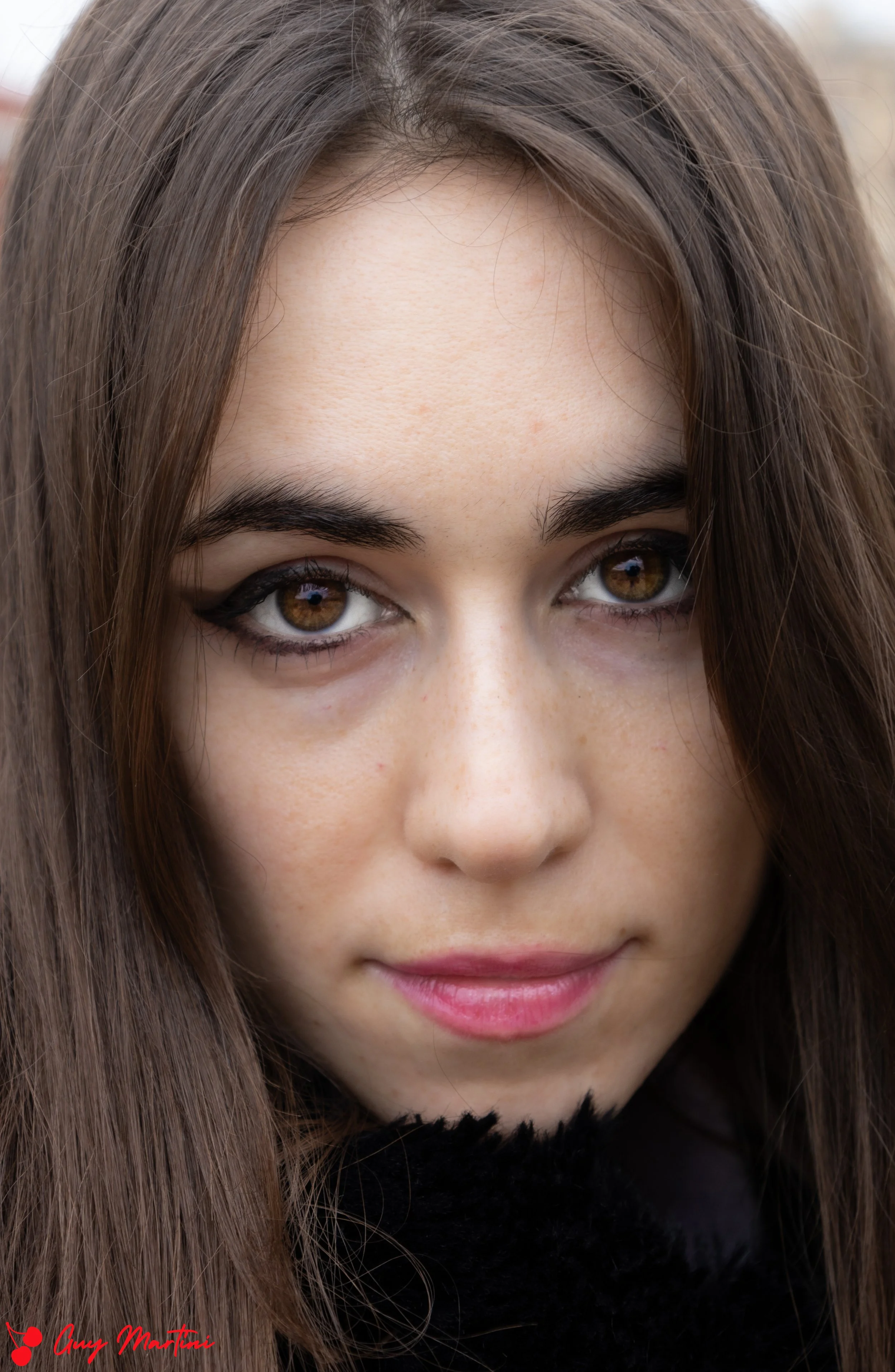  Primo piano di una giovane donna con capelli marroni e occhi marroni, che indossa un trucco scuro sugli occhi e un sorriso leggero.