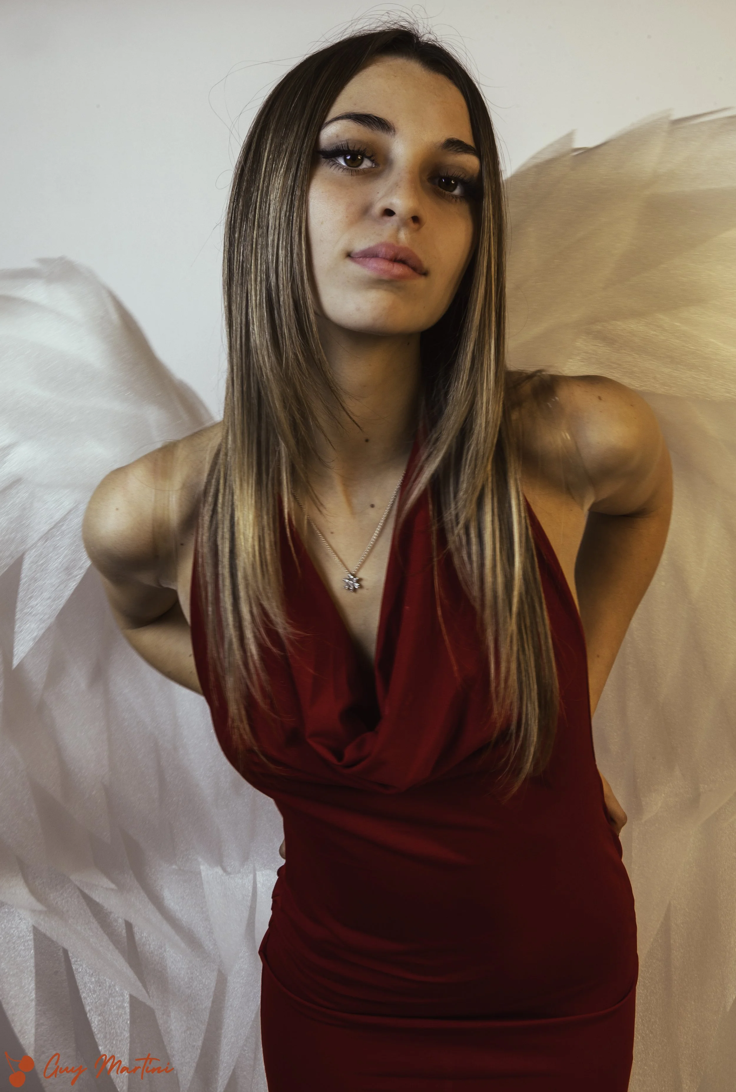 Donna con ali di fata in abito rosso con sfondo chiaro.