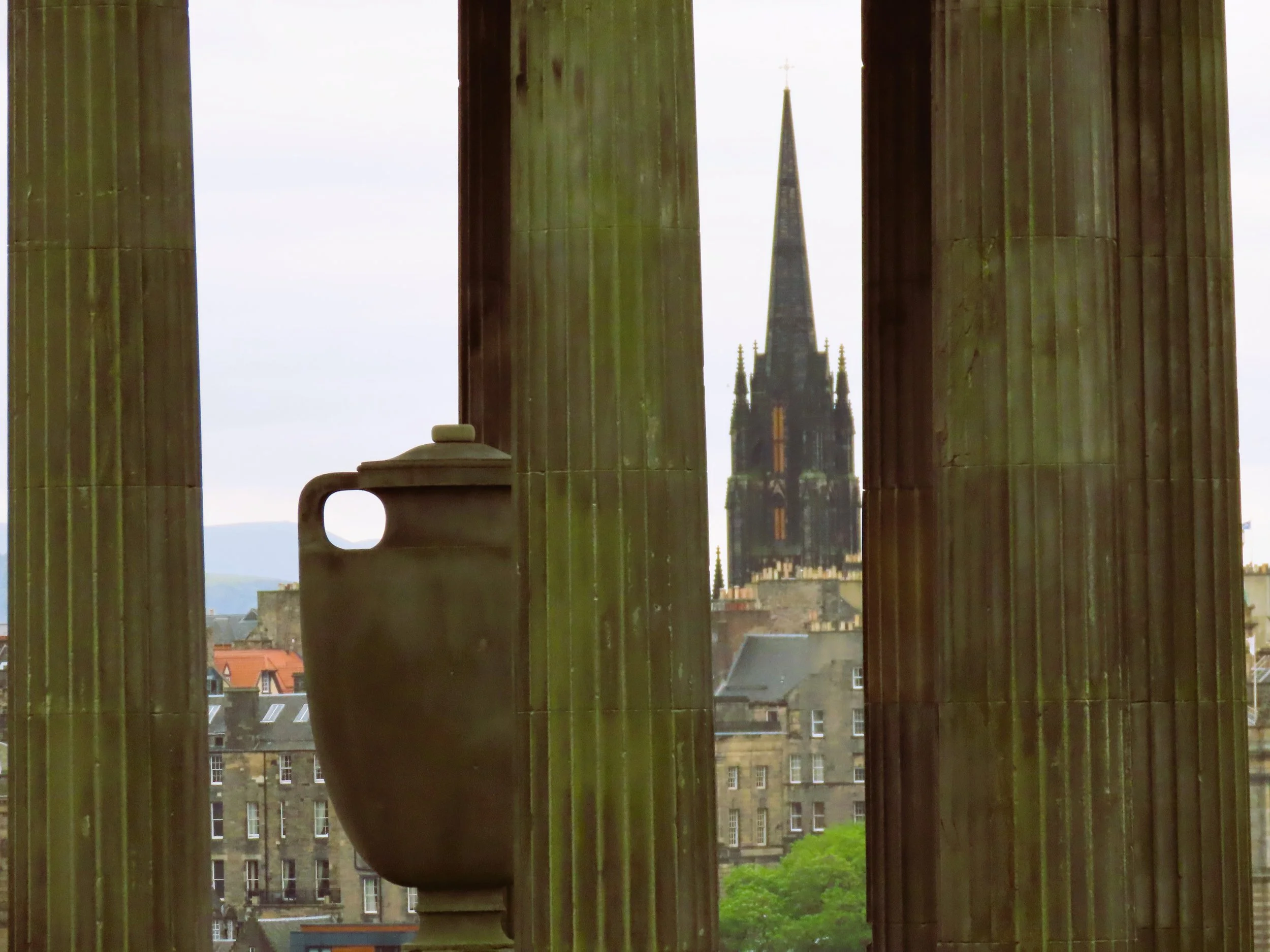 Vista di una chiesa con alta torre, vista tra colonne di un edificio, con un grande vaso in primo piano.