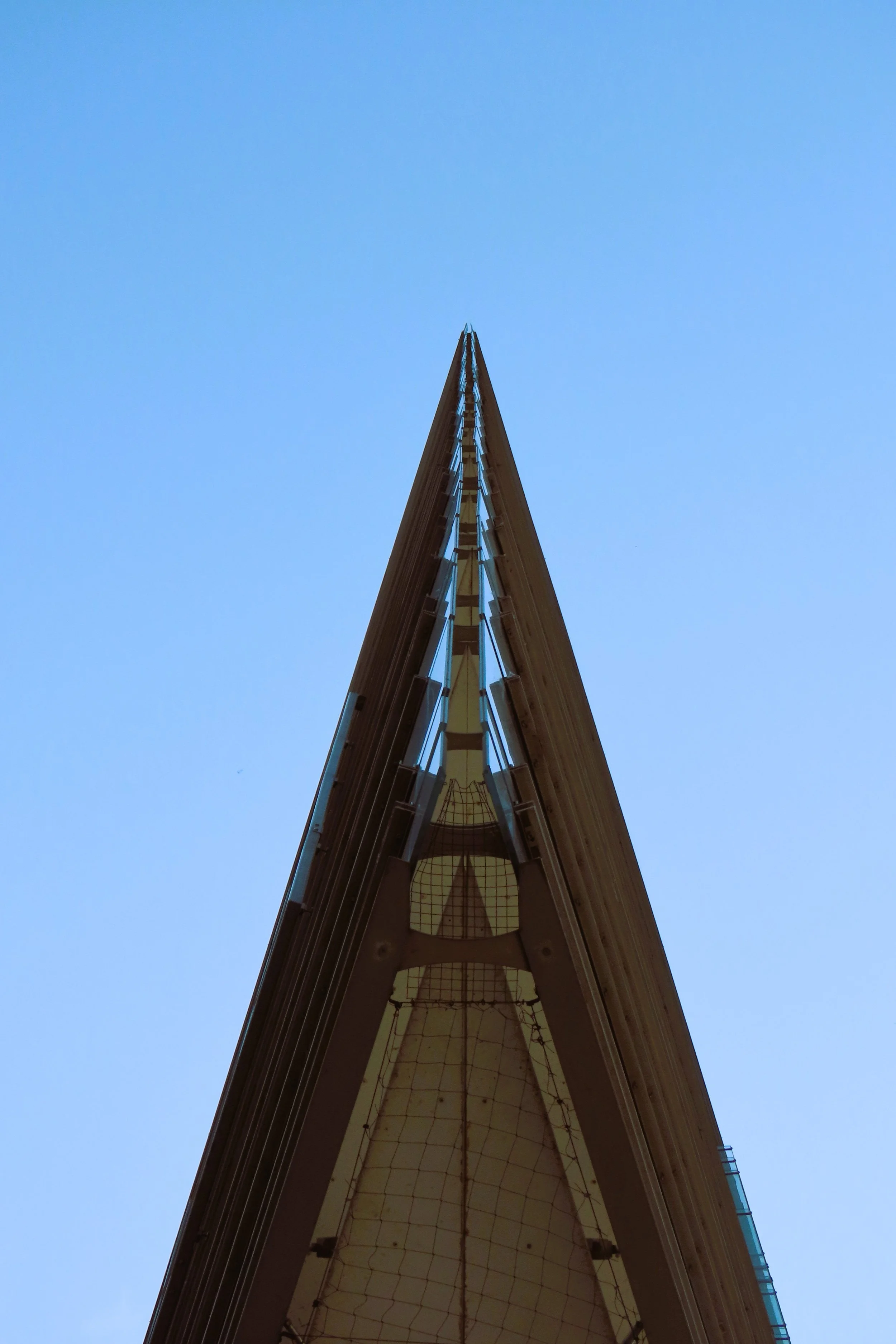 Vista dal basso di un edificio moderno rivolto verso il cielo blu, con linee architettoniche affilate e una facciata in vetro.