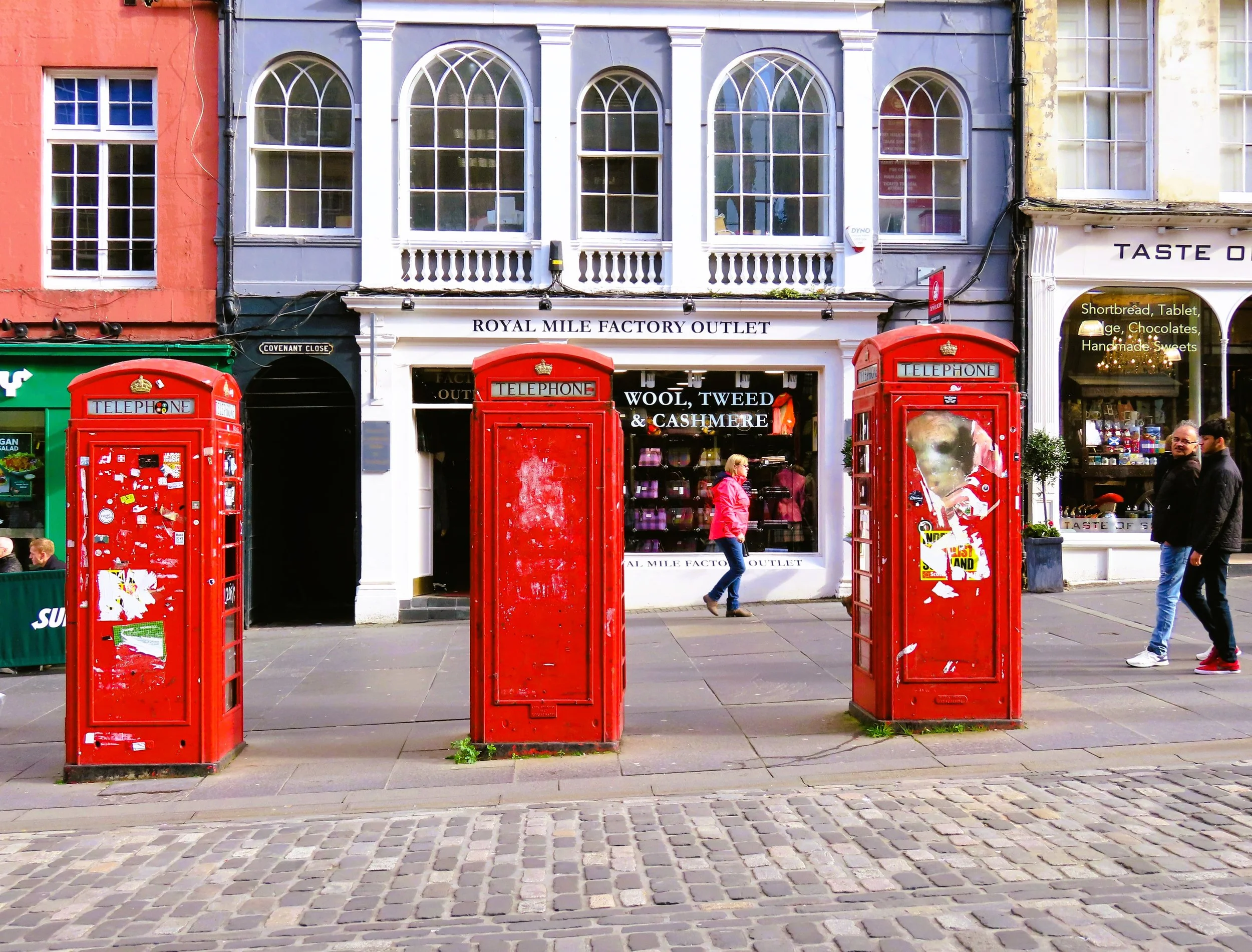 Tre cabine telefoniche rosse su un marciapiede di strada con negozi sullo sfondo.