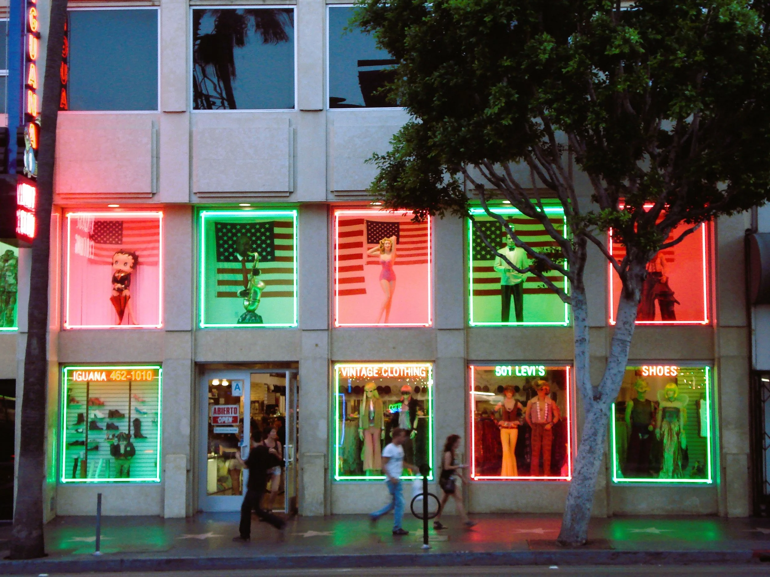 Vetrina luminosa di un negozio con manichini vestiti e neon colorati.