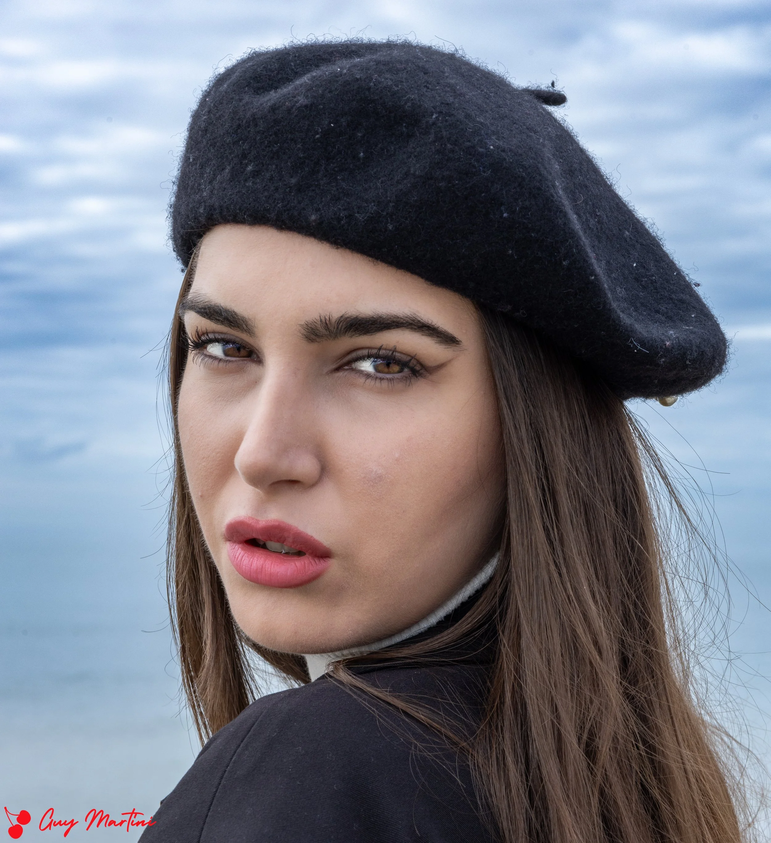 Ragazza con cappello nero in mare, sfondo nuvoloso.