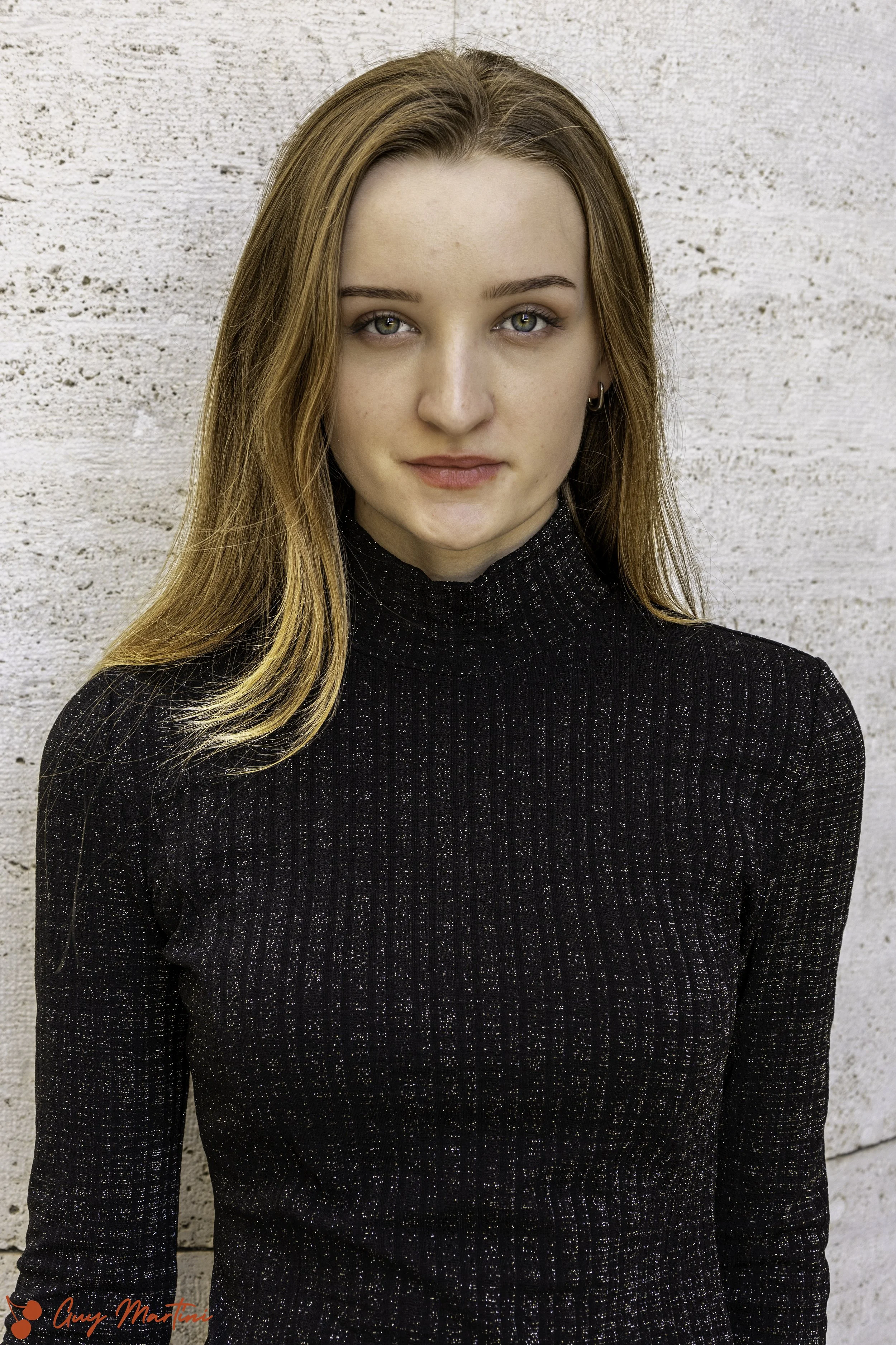 Ragazza con capelli castani e occhi verdi all'aperto, indossa un maglione nero con dettagli brillanti, sfondo bianco.