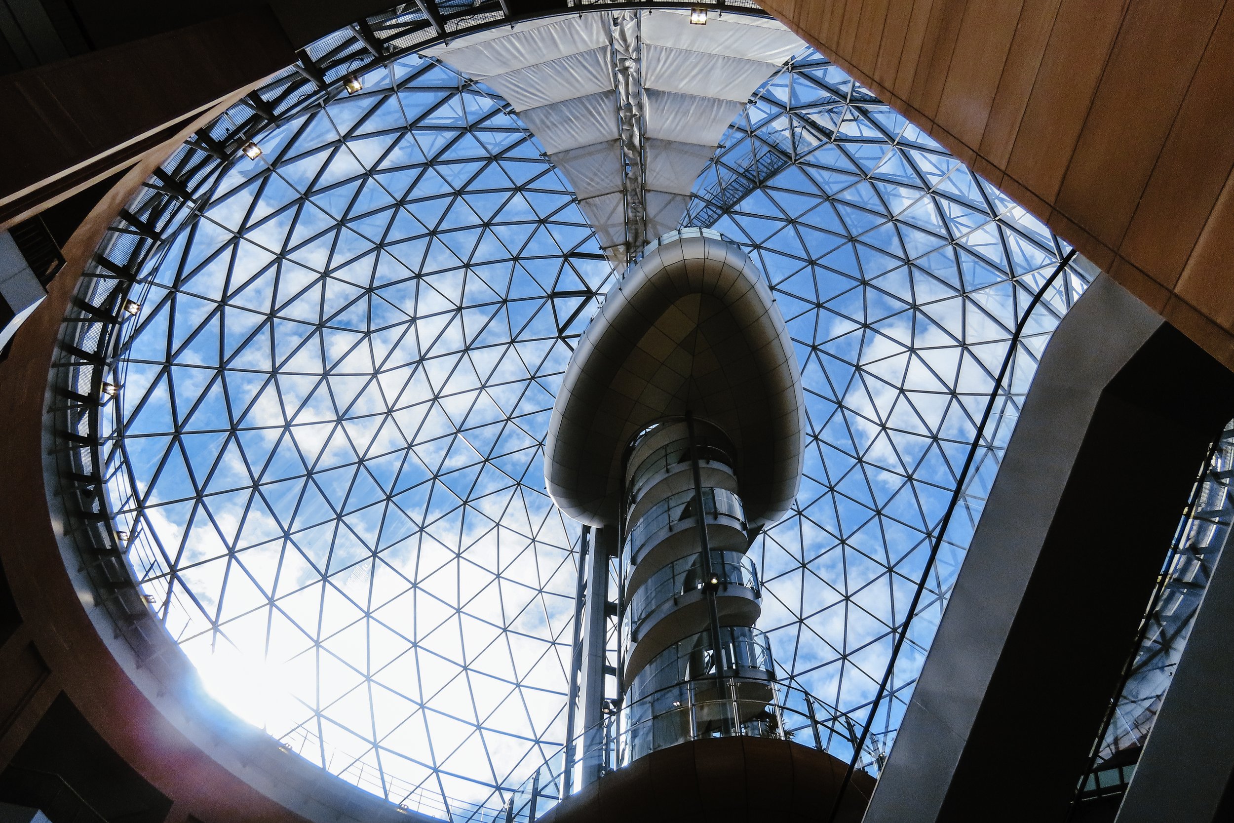 Interno di un edificio con una grande cupola in vetro e un ascensore trasparente al centro