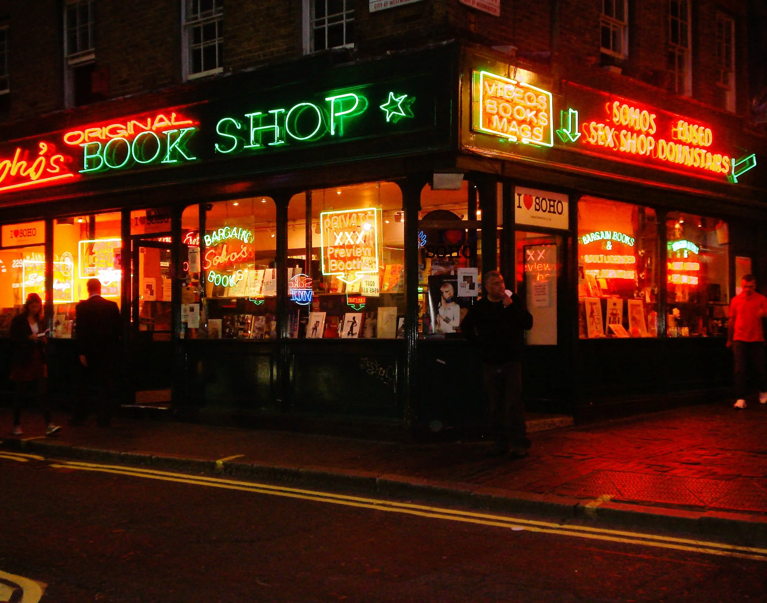 Libreria con insegne al neon colorato intorno a una strada, con molte persone fuori, di sera.