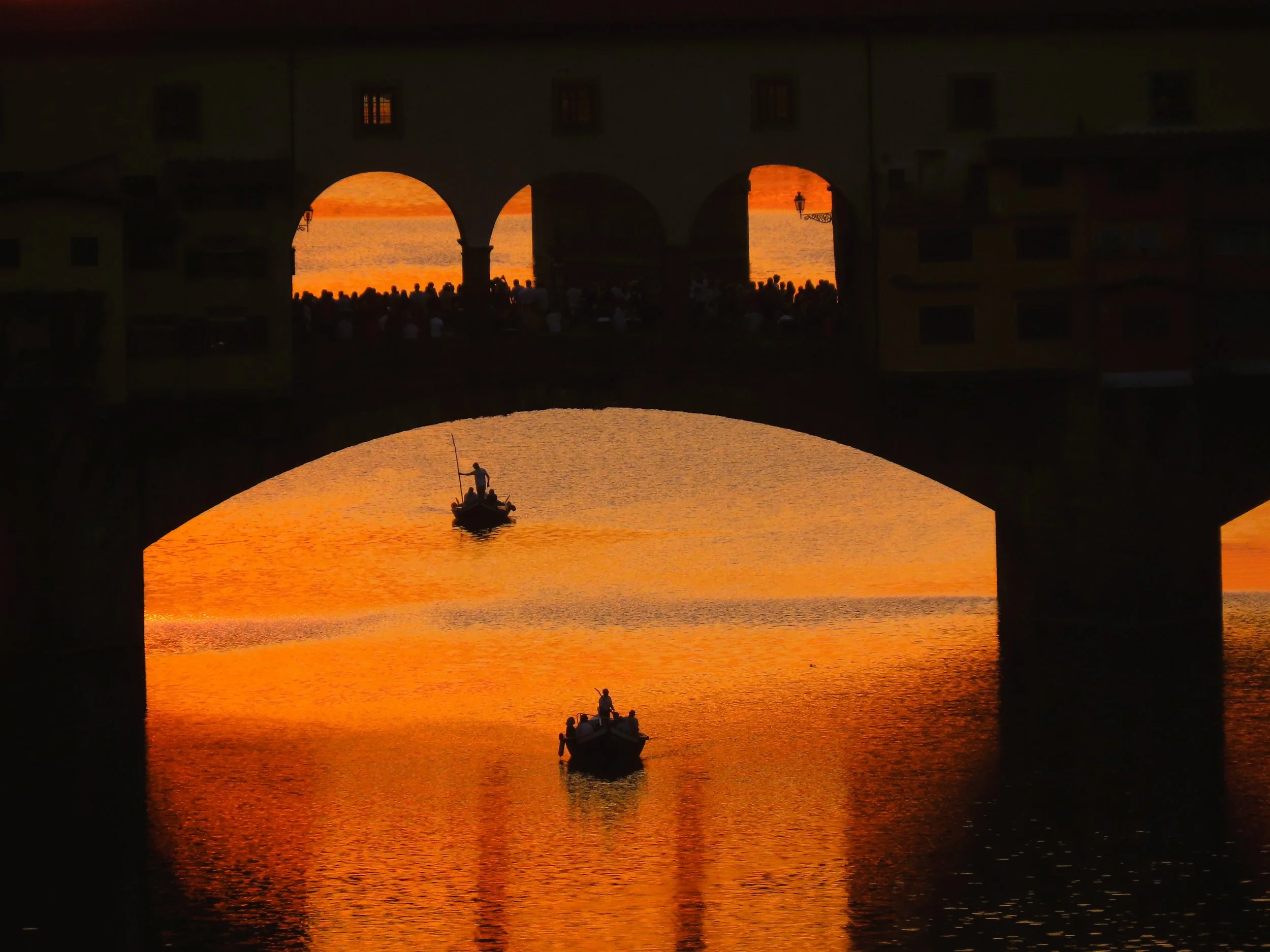 Due barche con persone al tramonto sotto un ponte con archi, reflect manier da acqua calma e cielo arancione