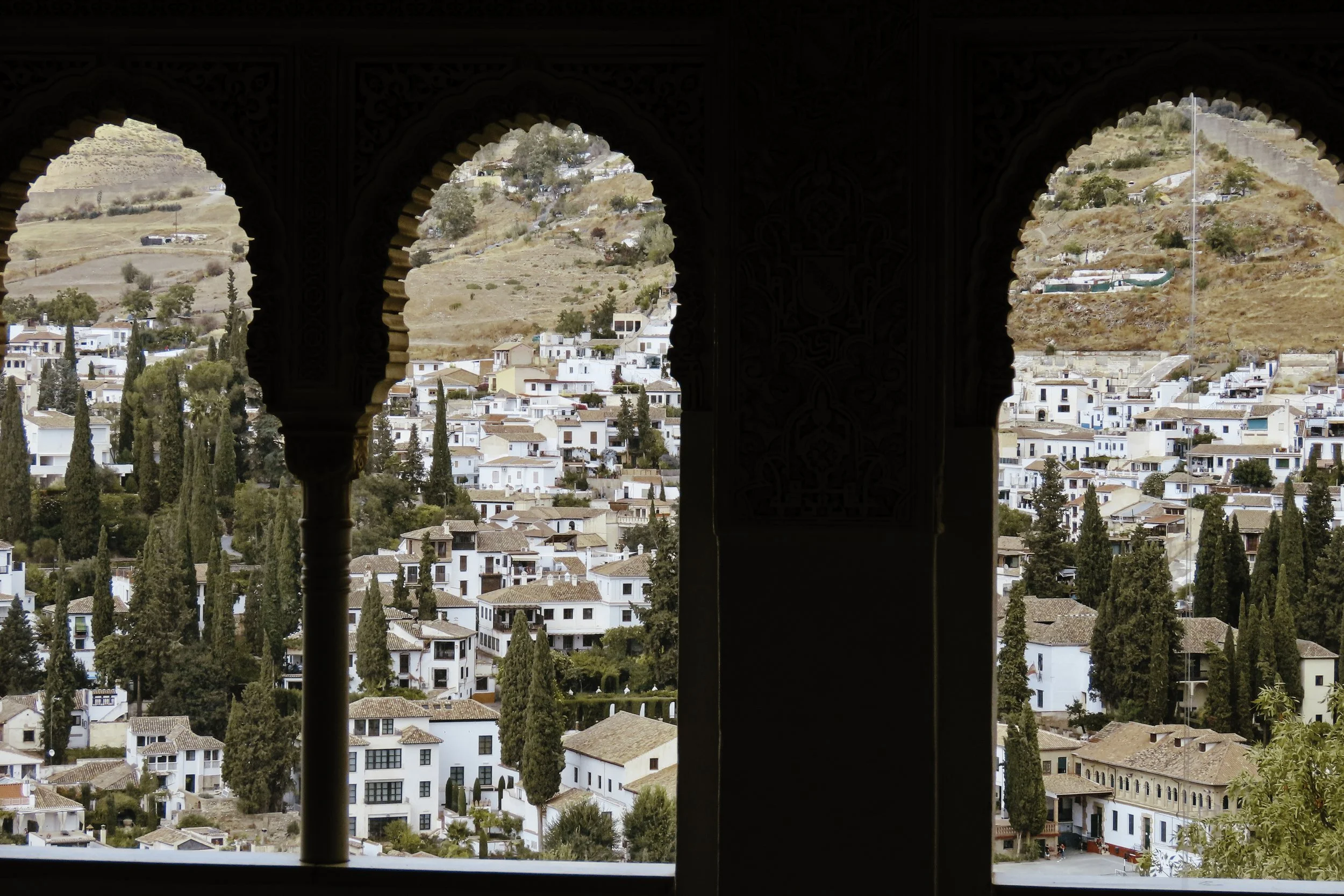 Vista di un villaggio bianco con case e cipressi, vista attraverso archi decorativi in stile moresco.