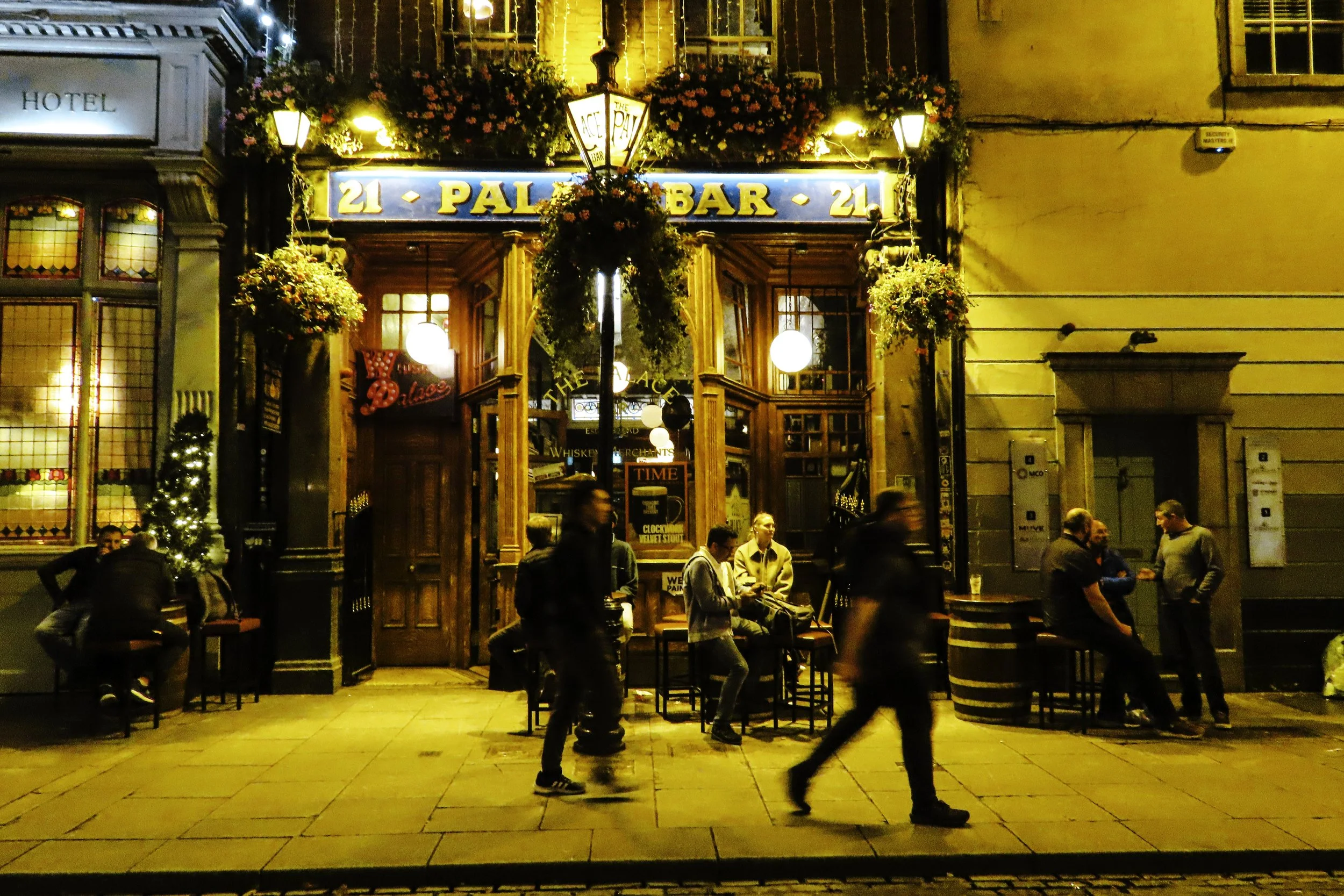 Esterno di un pub accogliente con persone sedute e in piedi all'ingresso, decorazioni natalizie e luci calde in una strada di sera in Italia.