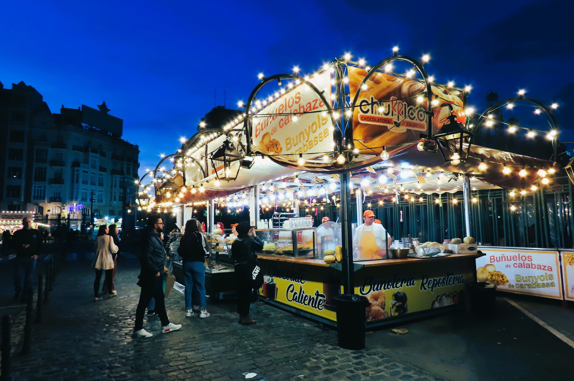 stall di cibo con luci decorative in una piazza affollata di persone di sera