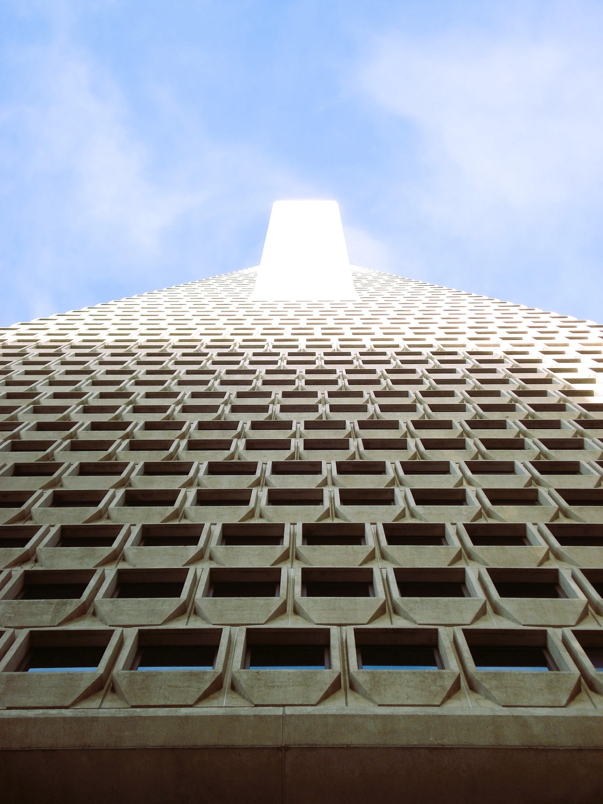 Vista dal basso di un grattacielo con una facade di pattern geometrico quadrato, verso il cielo.
