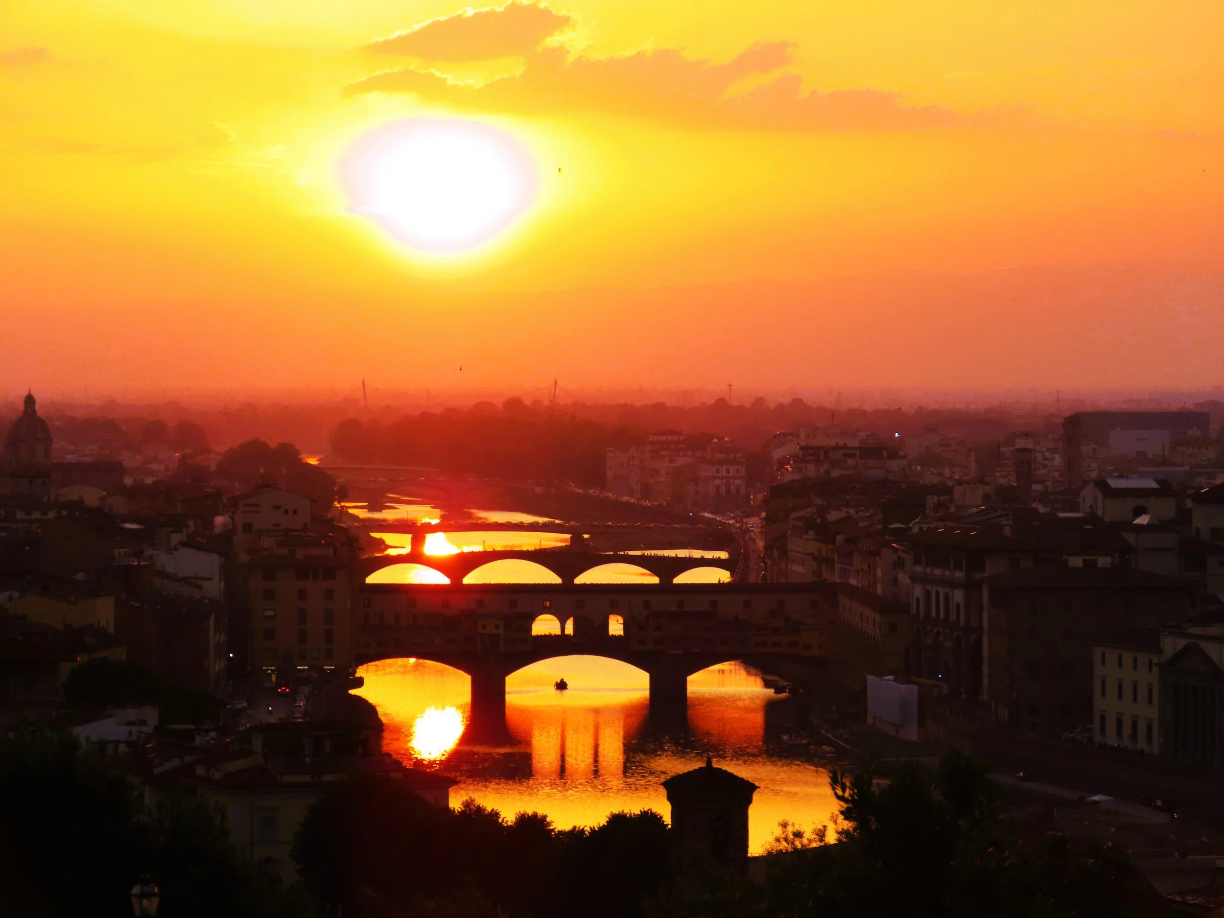 Tramonto sul fiume con ponti, città e cielo arancione e giallo.