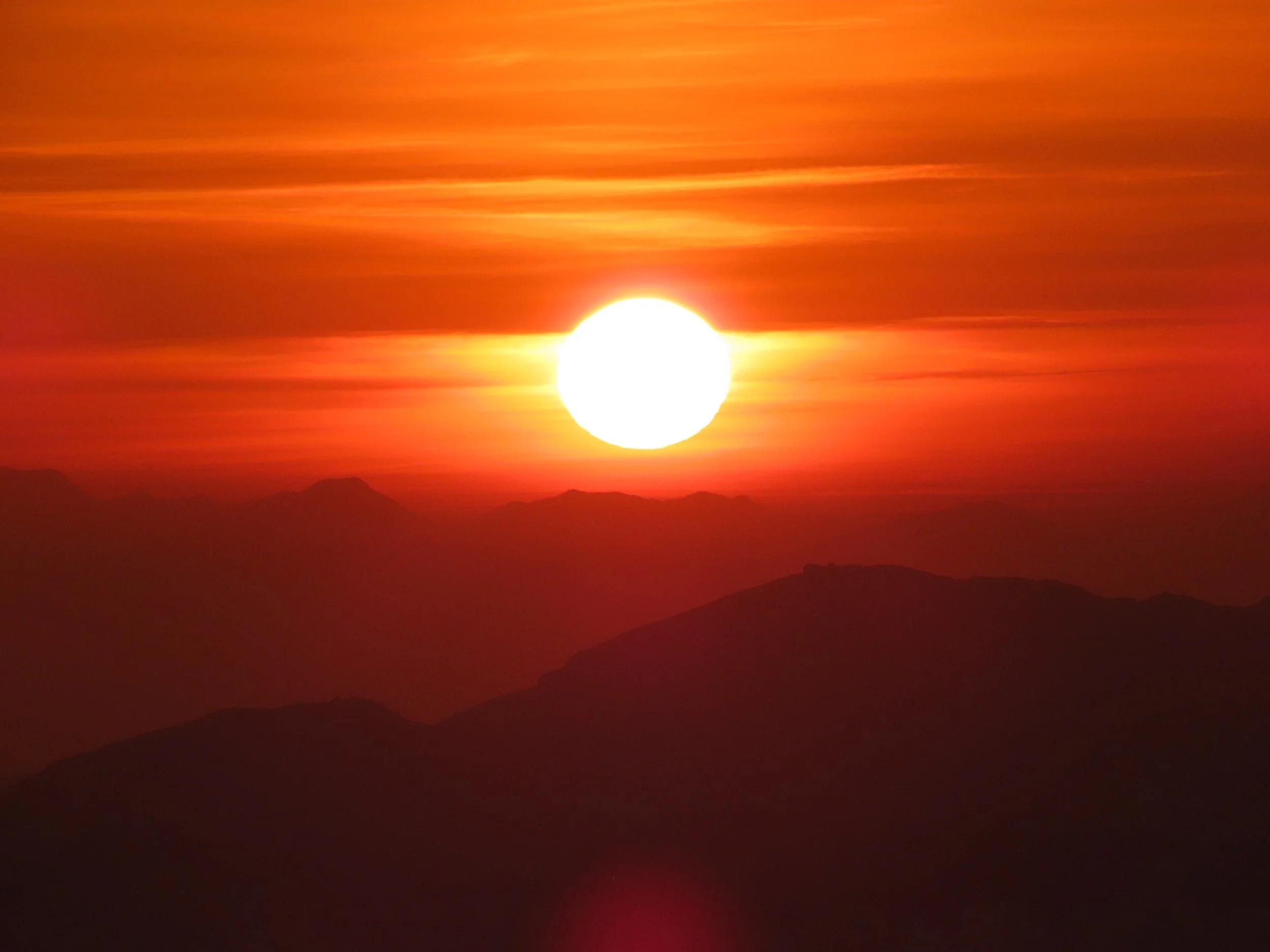 Sole al tramonto sopra le montagne con cielo arancione e nuvole.
