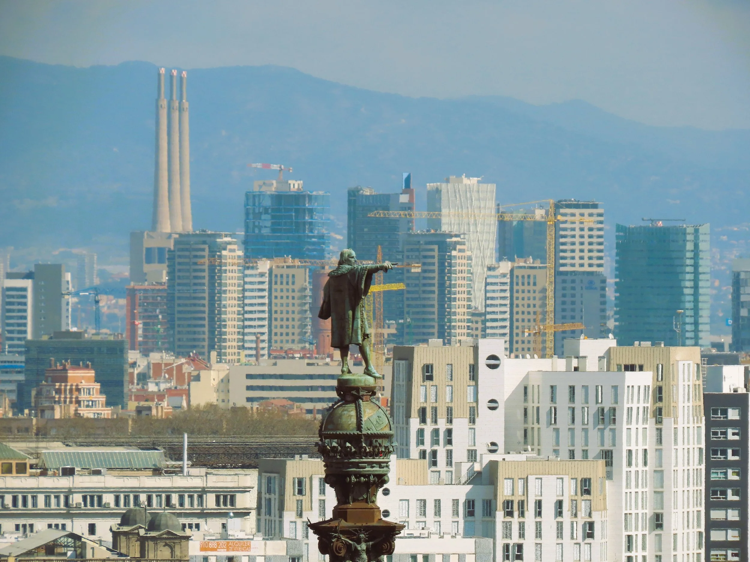 Statua di Vittorio Emanuele II in cima a un monumento con un panorama di grattacieli di una città, con montagne sullo sfondo.