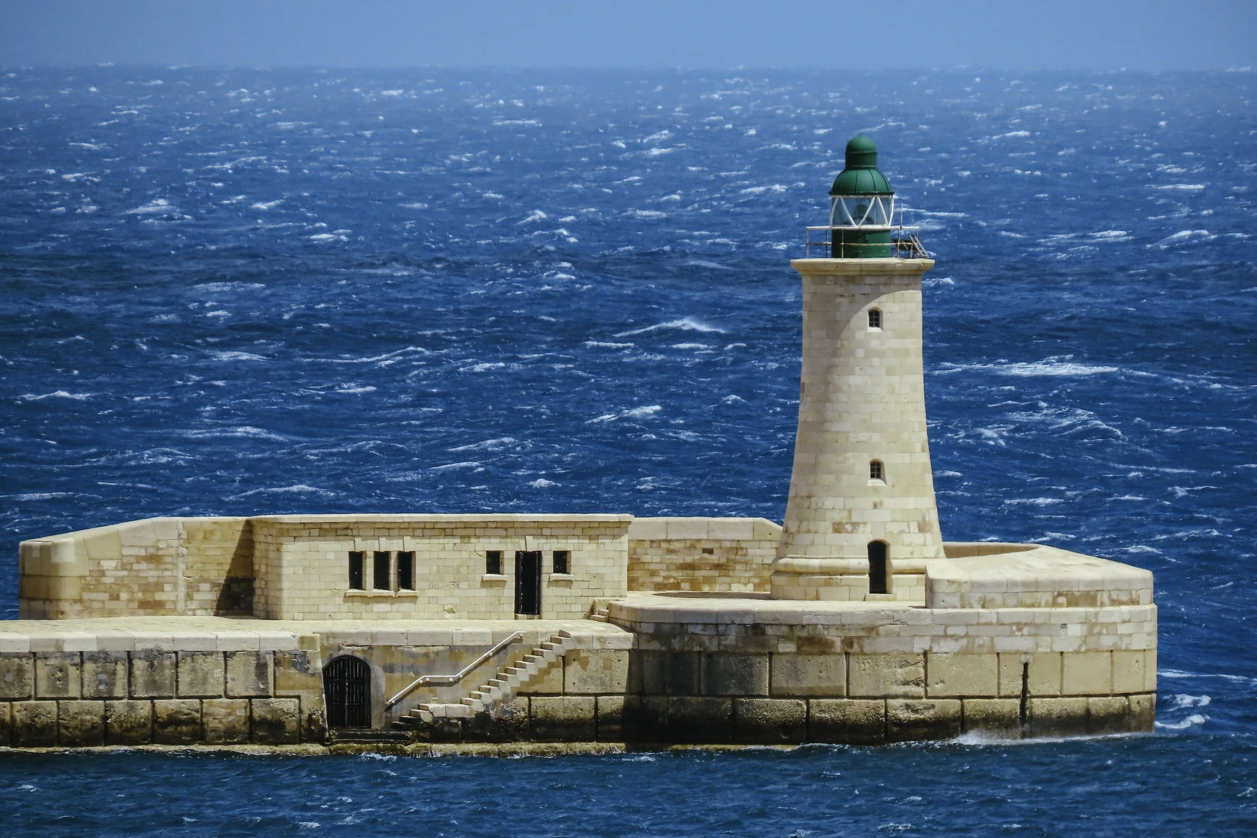 Faro di pietra sulla spiaggia con mare blu intenso sullo sfondo.