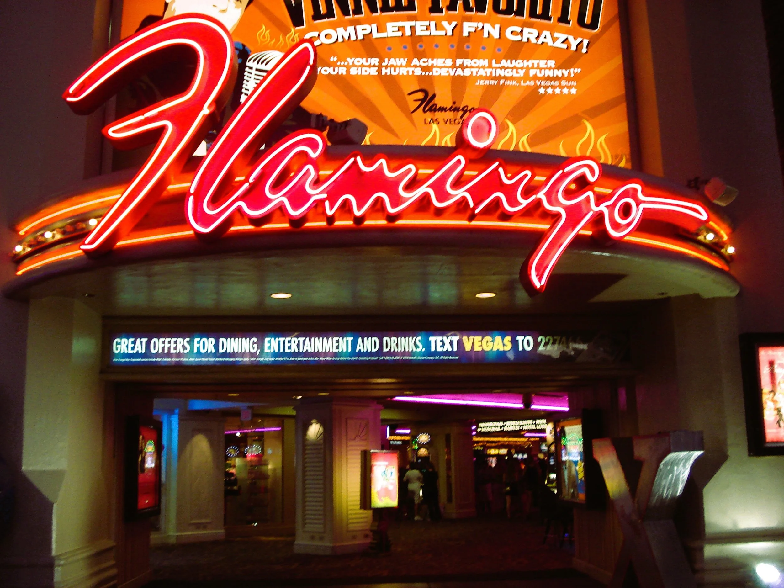 Ingresso di un casinò con una grande insegna neon rossa con scritto 'Flamingo' e un pannello digitale con offerte e promozioni.