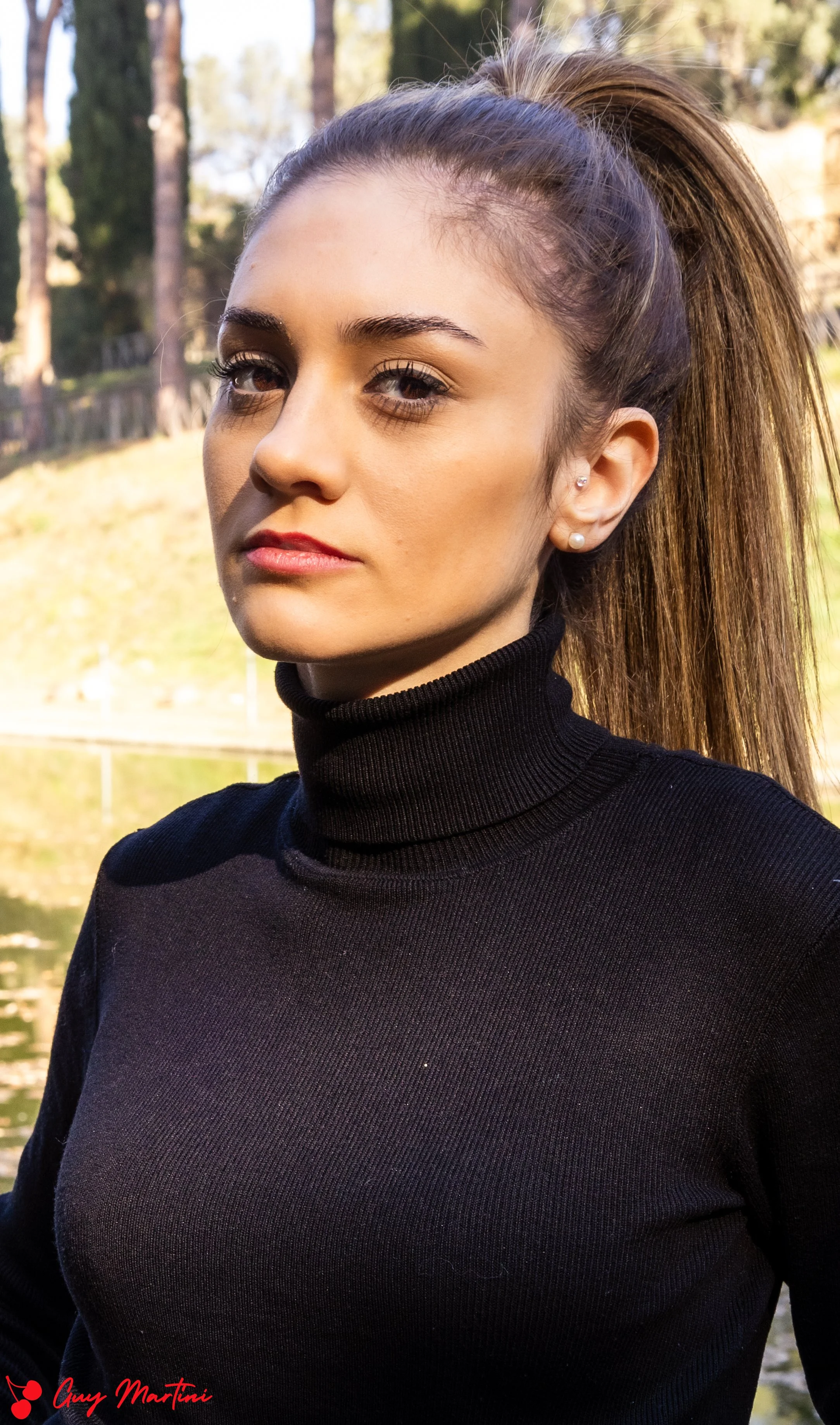 Ragazza con foulard nero e orecchini di perle, sfondo naturale con acqua e alberi, luce del tramonto
