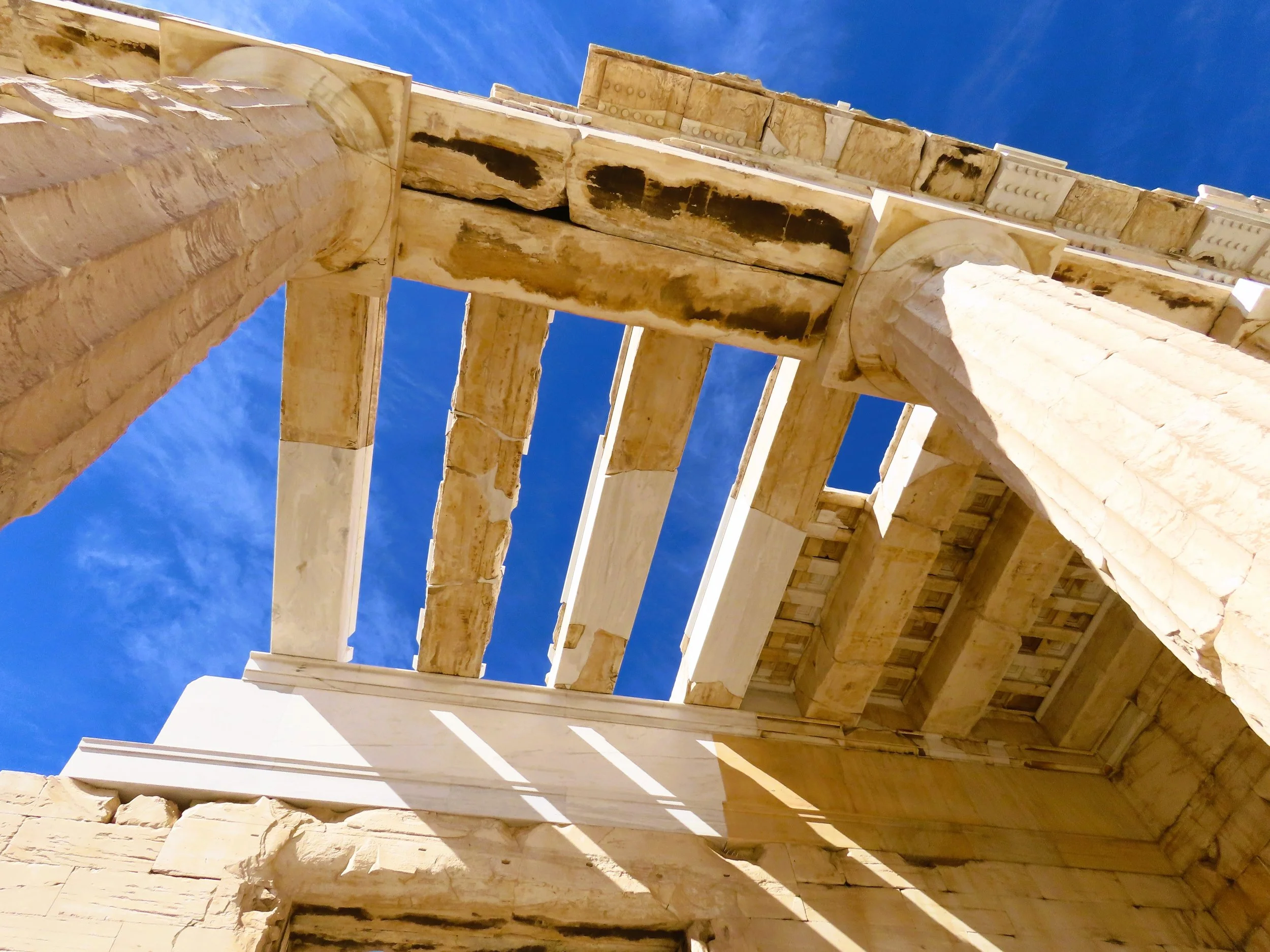Vista dall'alto di antiche colonne e resti di un tempio greco in marmo, con il cielo blu sullo sfondo.